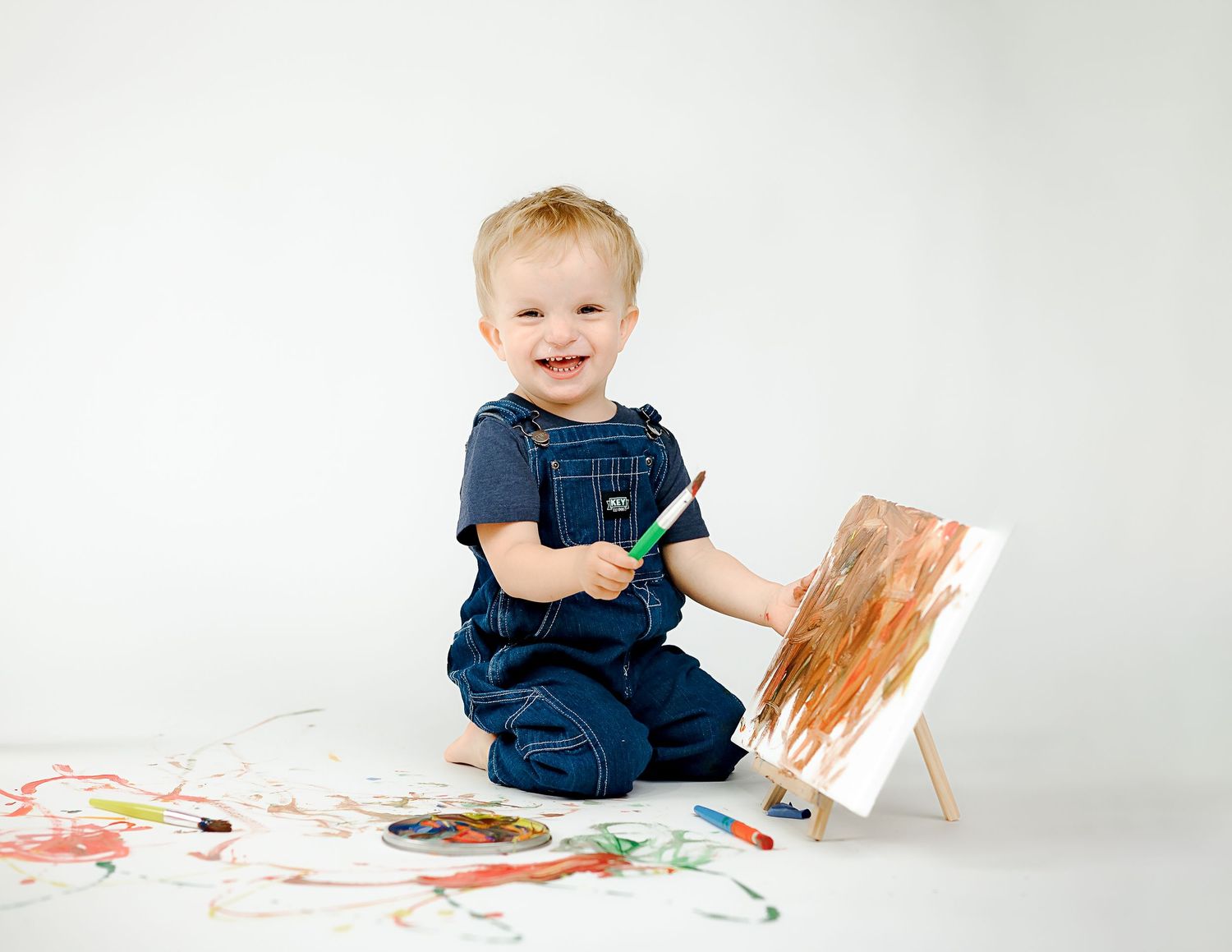 Child in navy blue outfit painting with bright colors on white paper.