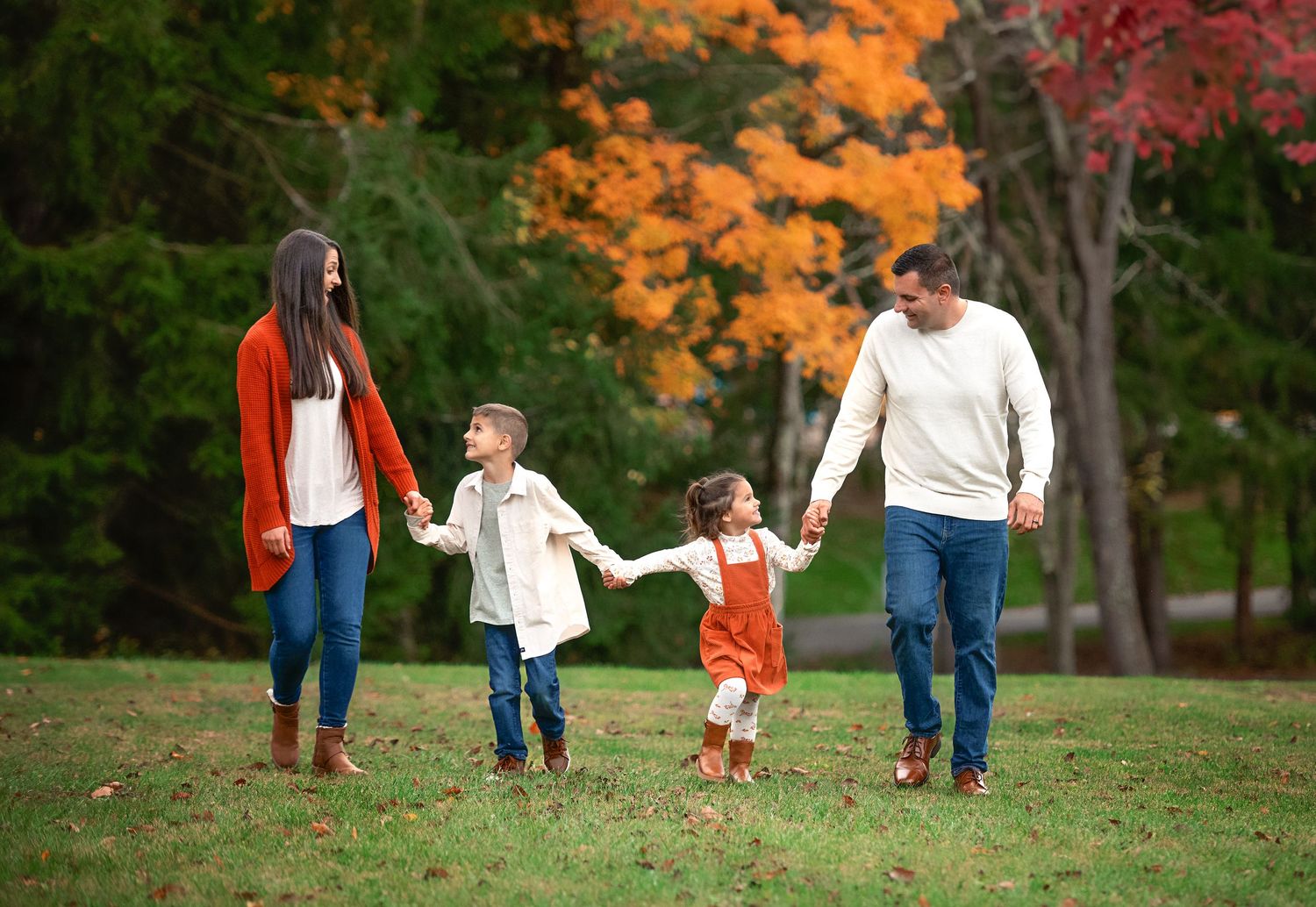 A family holds hands while walking through a park with beautiful fall colors.