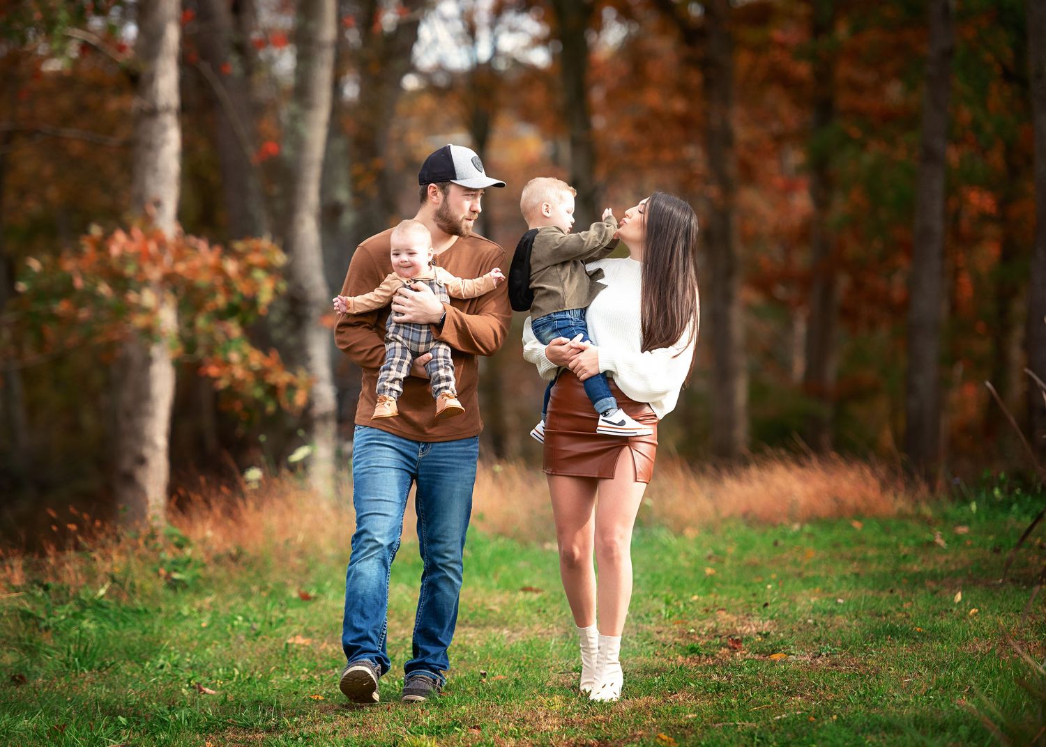 A couple walks together through a scenic autumn forest holding their children.