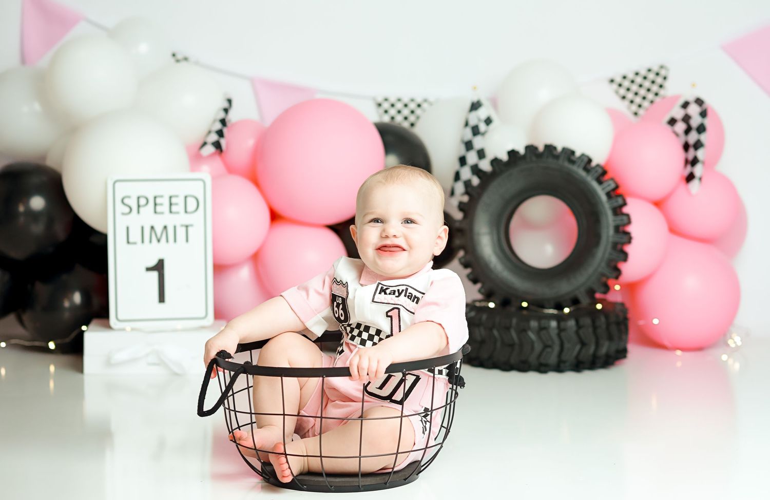 Racing themed baby photo setup with pink balloons, tires and checkered flags.