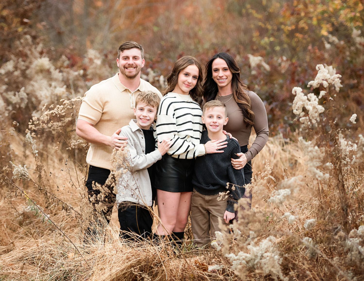 A family poses together among autumn foliage during a golden hour photoshoot.