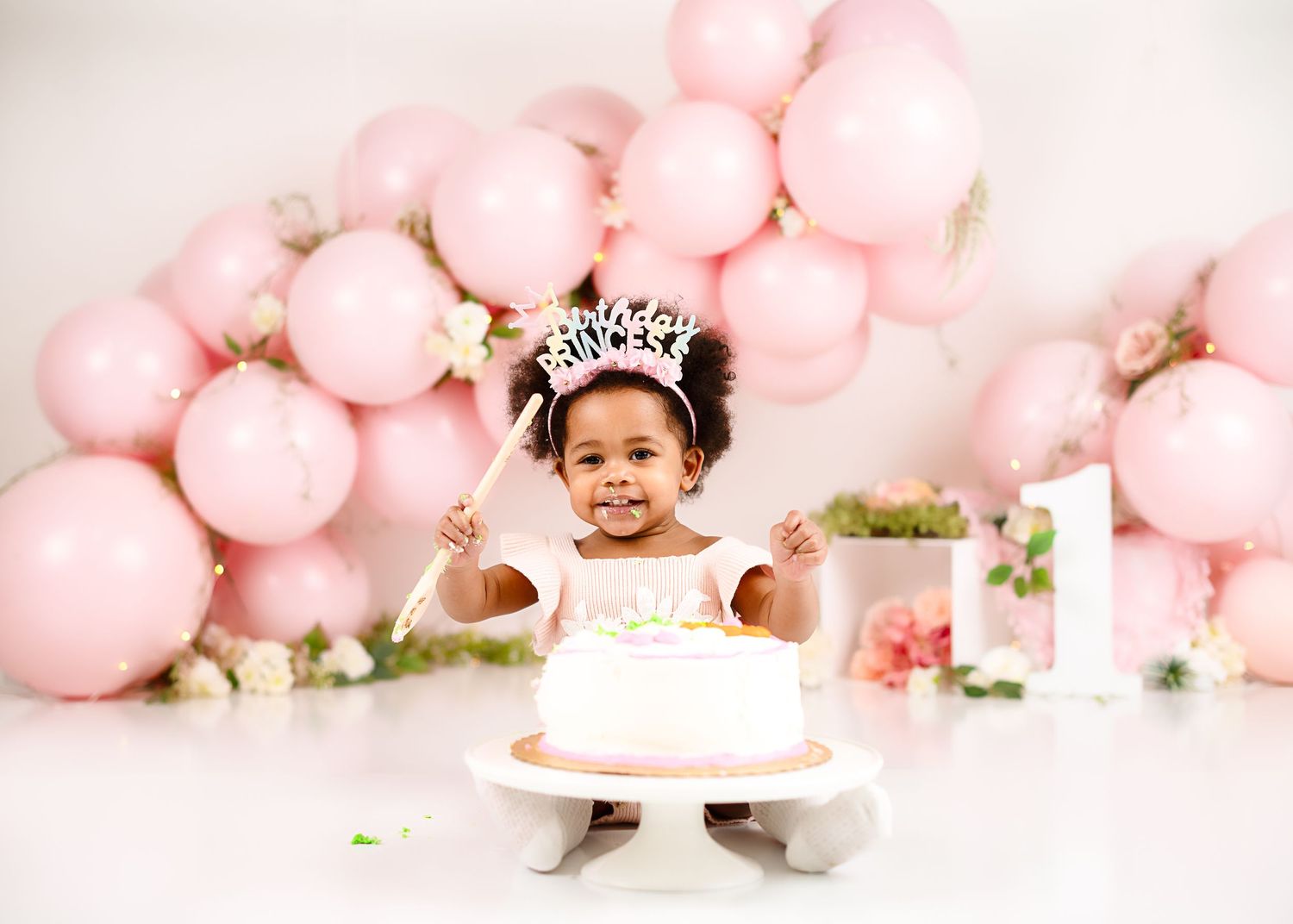 Pink balloon and cake smash photography setup with floral decorations.