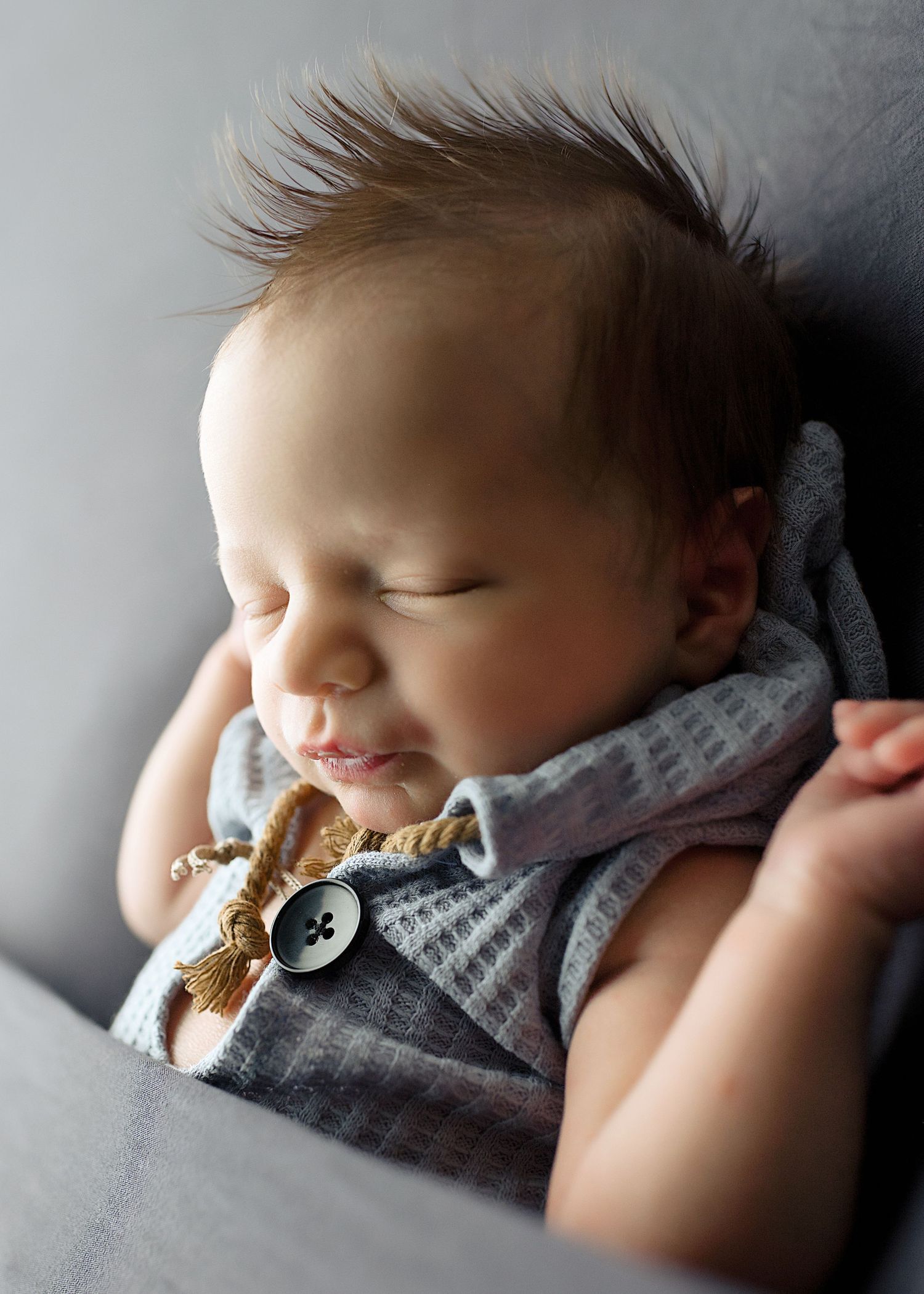 Sleeping baby in gray outfit with pacifier rests peacefully.