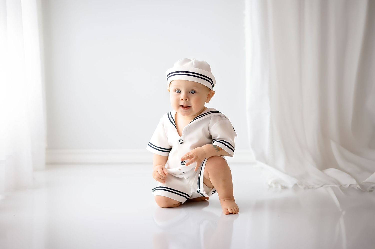Baby in white clothing lying on soft white blanket during milestone photography session.