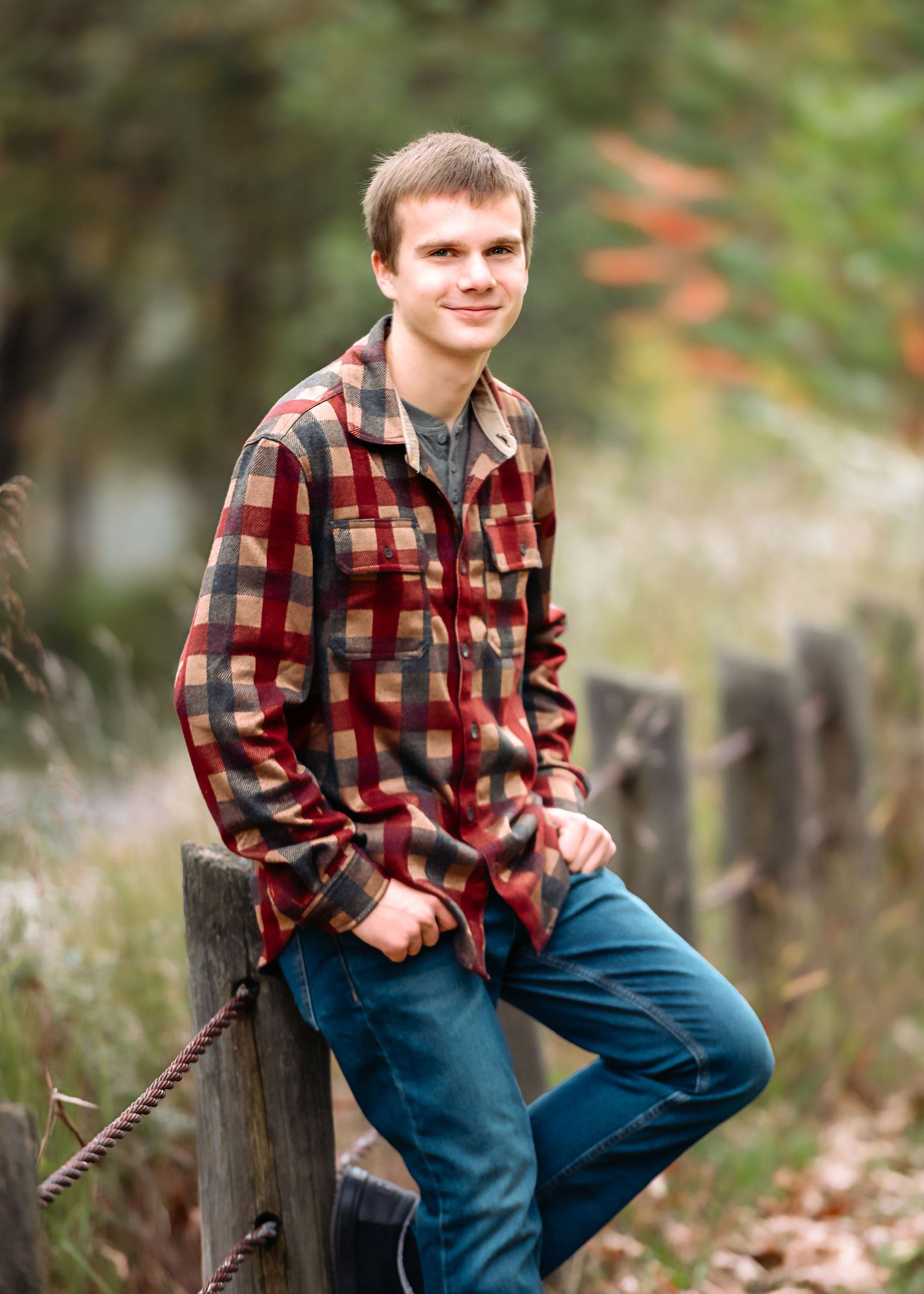 A casual portrait on wooden fence posts wearing a red plaid flannel shirt and jeans.