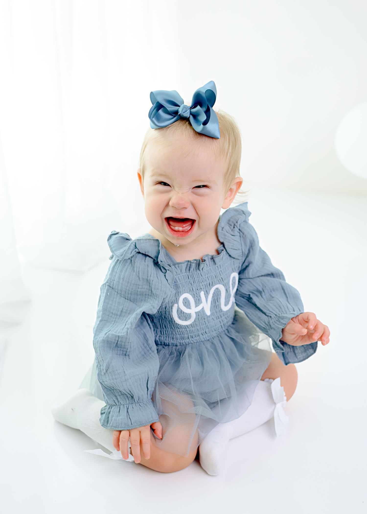 Baby photography session in blue ruffled outfit against white background.