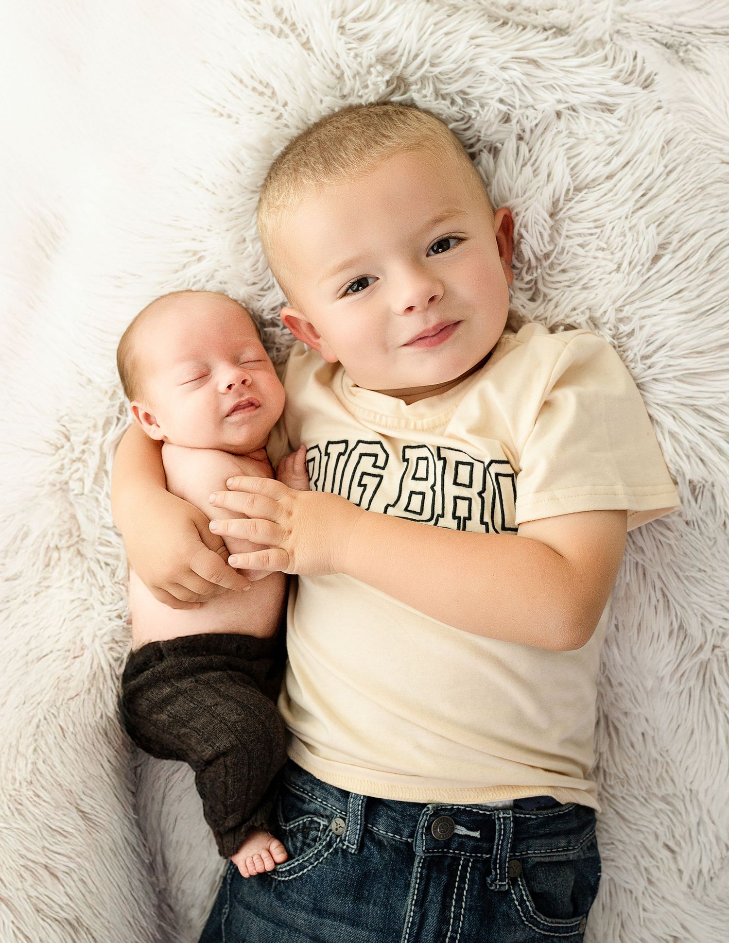 Two siblings lying on white fluffy rug wearing casual outfits during lifestyle photoshoot.