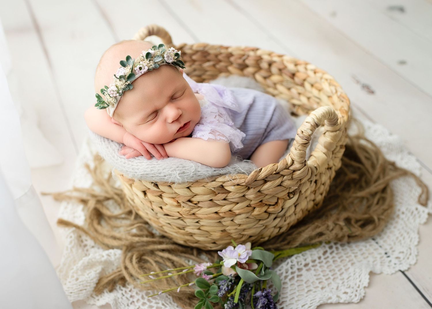 A baby sleeps peacefully in a woven basket decorated with delicate flowers and lace.