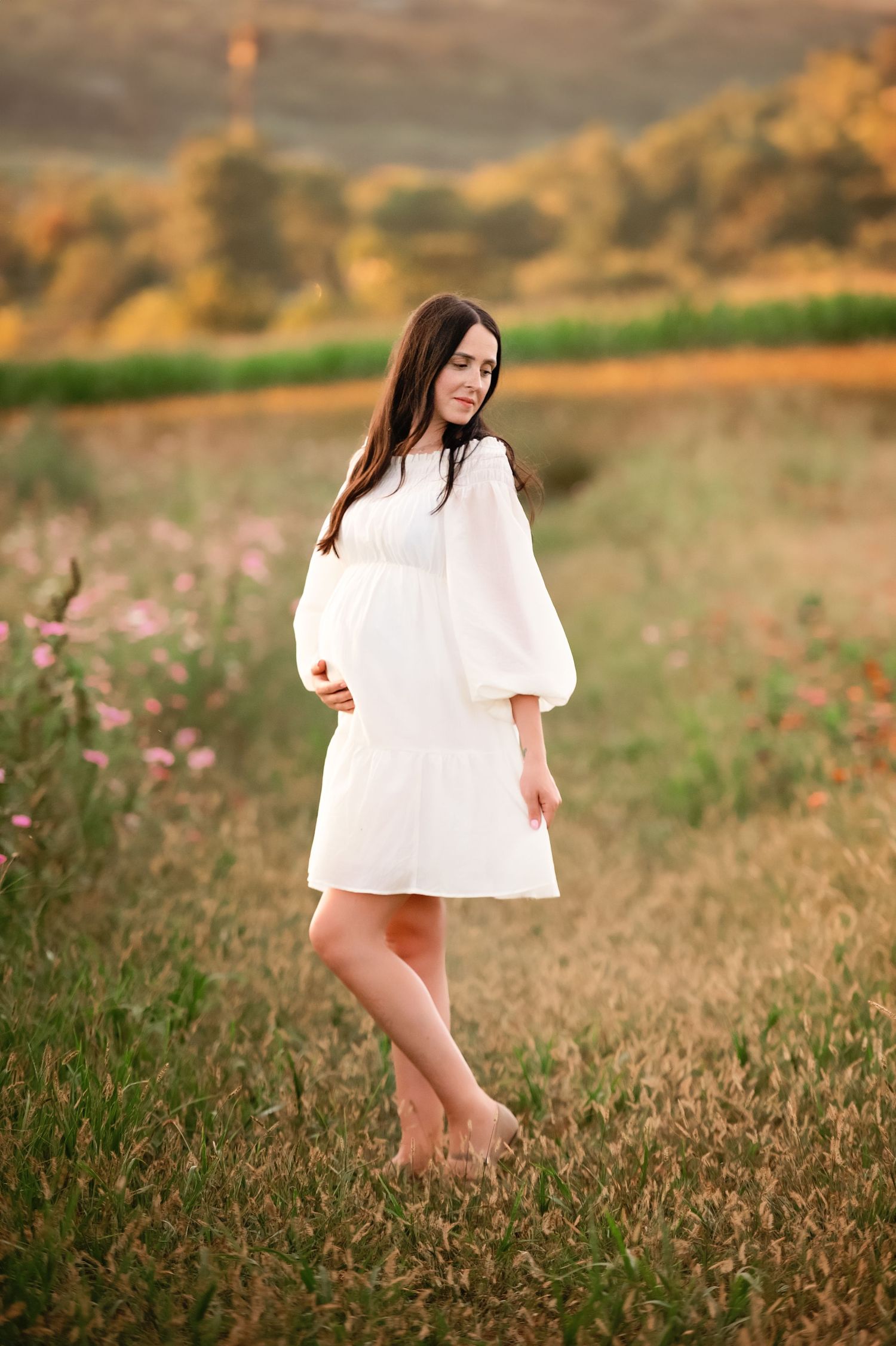 Figure in flowing white dress walking through a wild meadow at dusk.