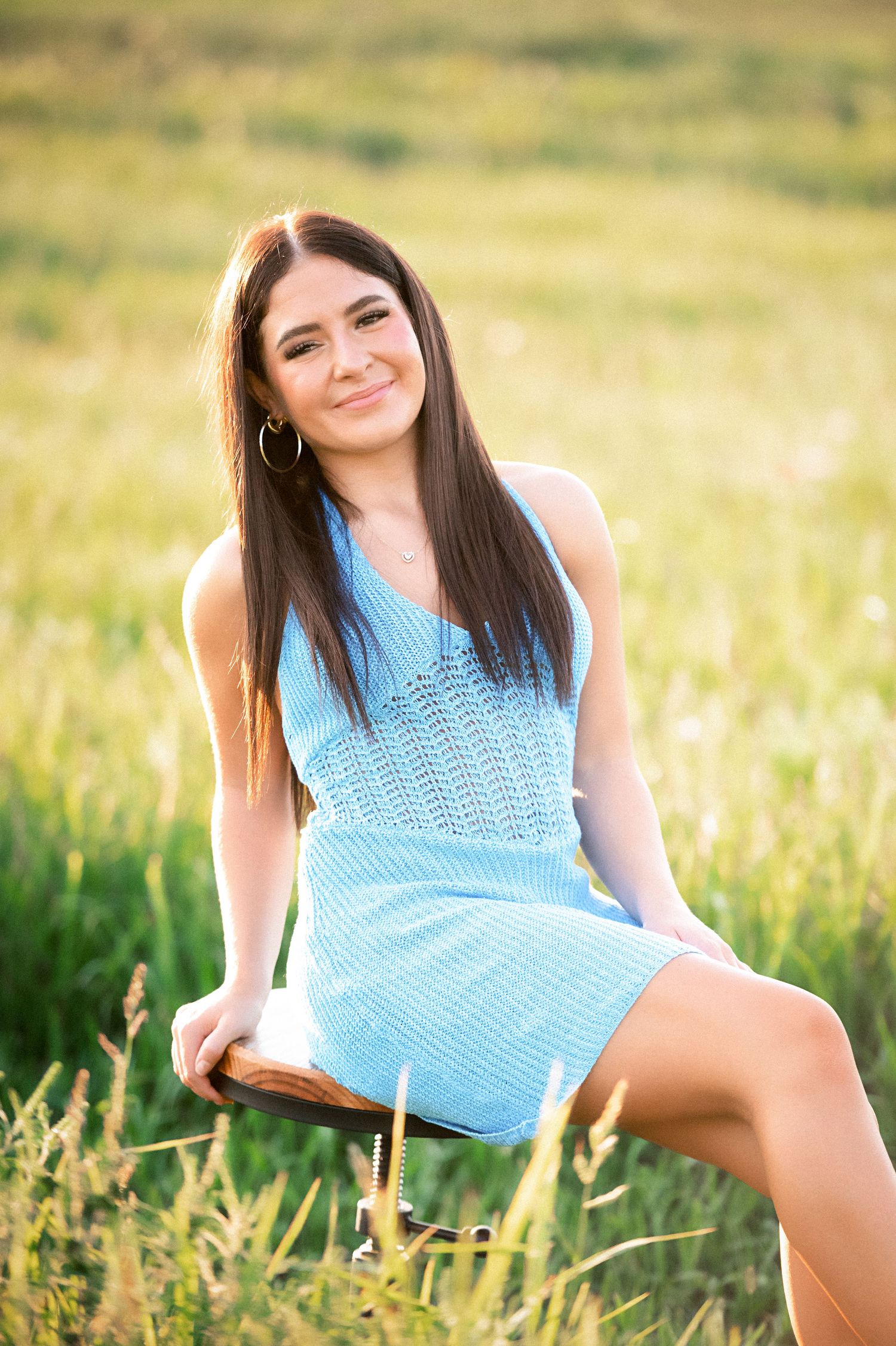 A person in a blue sleeveless top poses gracefully in a sun-lit meadow with tall grass.