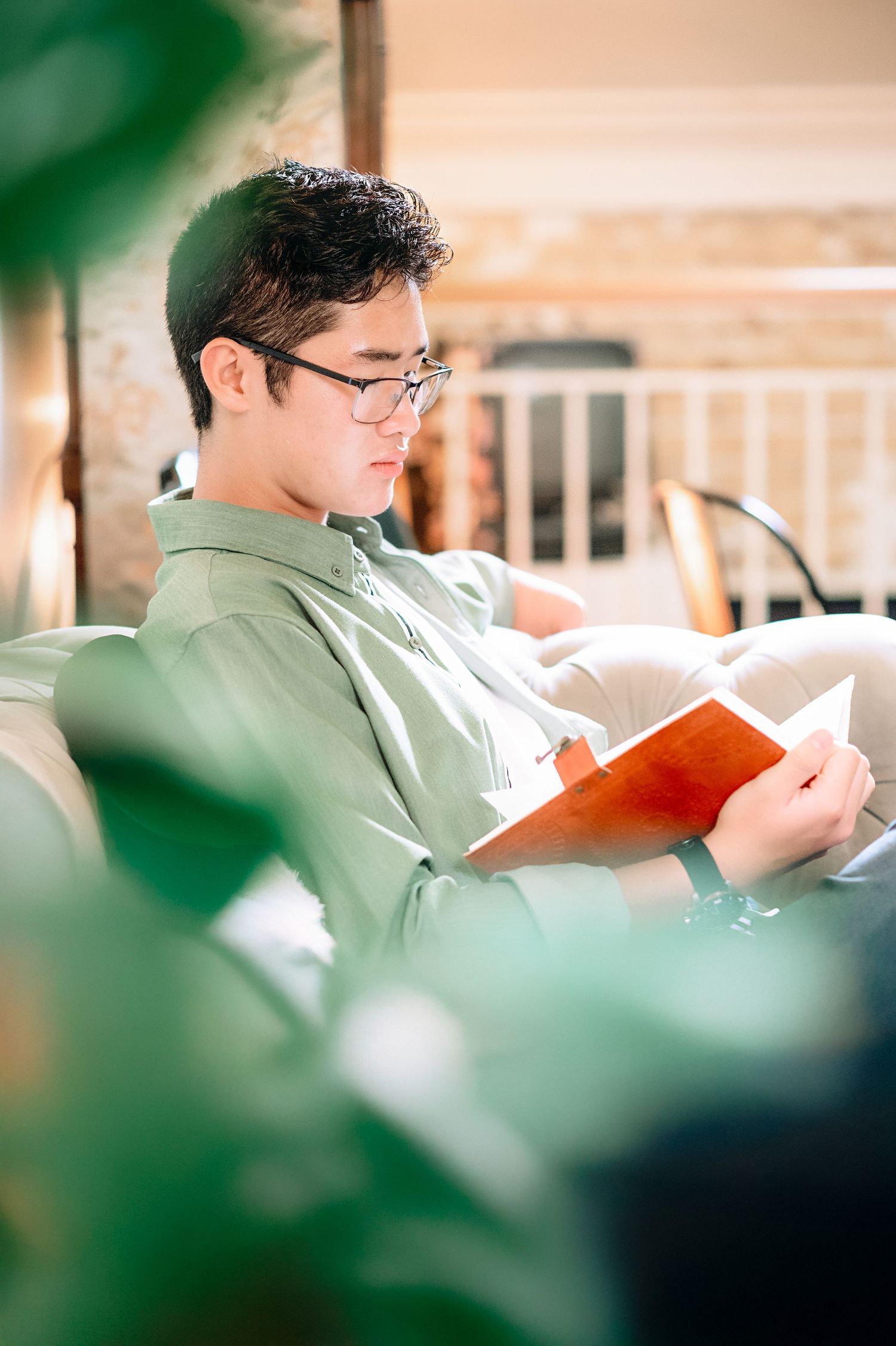 Person in green shirt reads book while relaxing in comfortable chair.