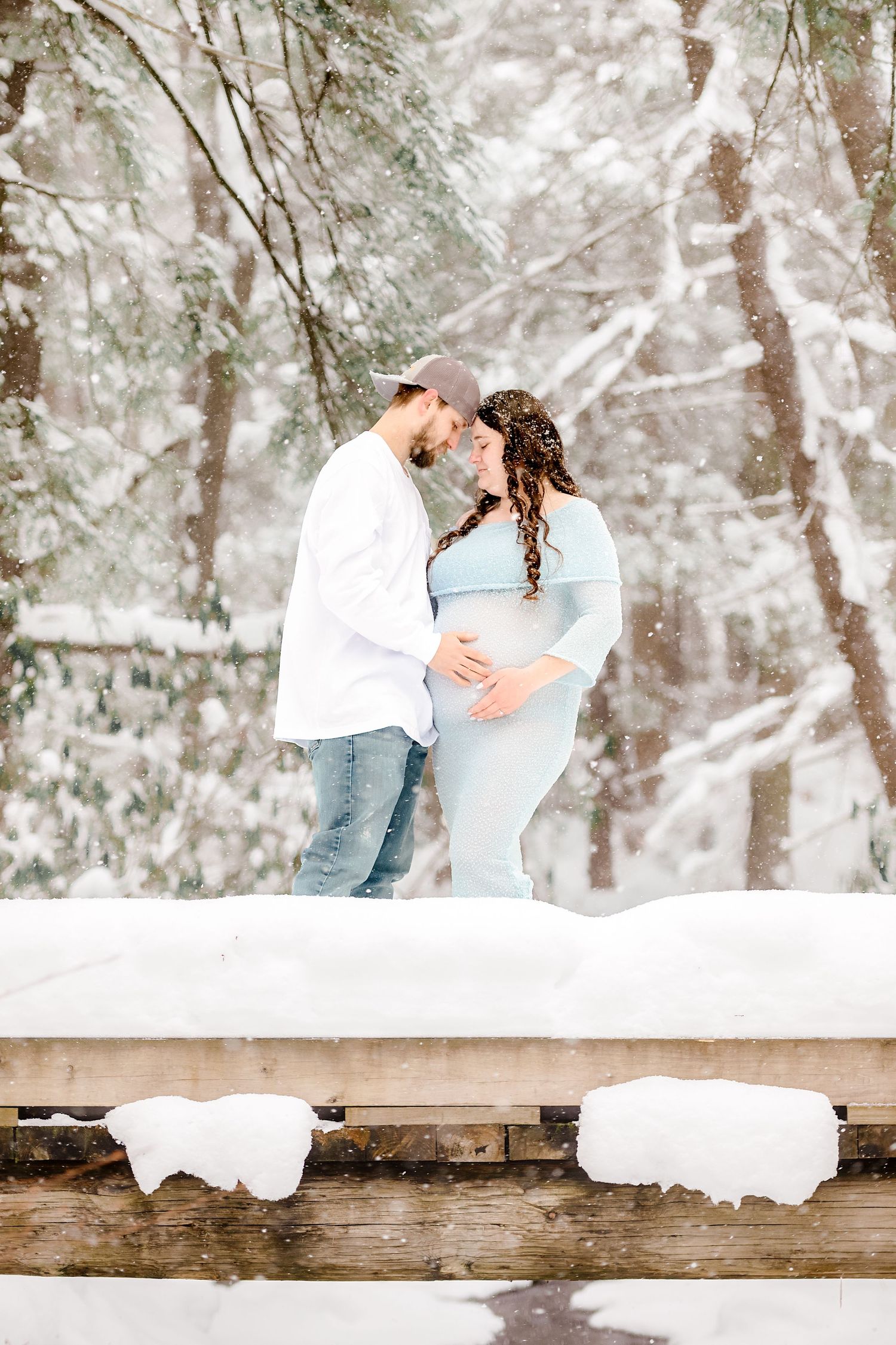 Winter engagement photos in a snowy forest with rustic wooden bench details.