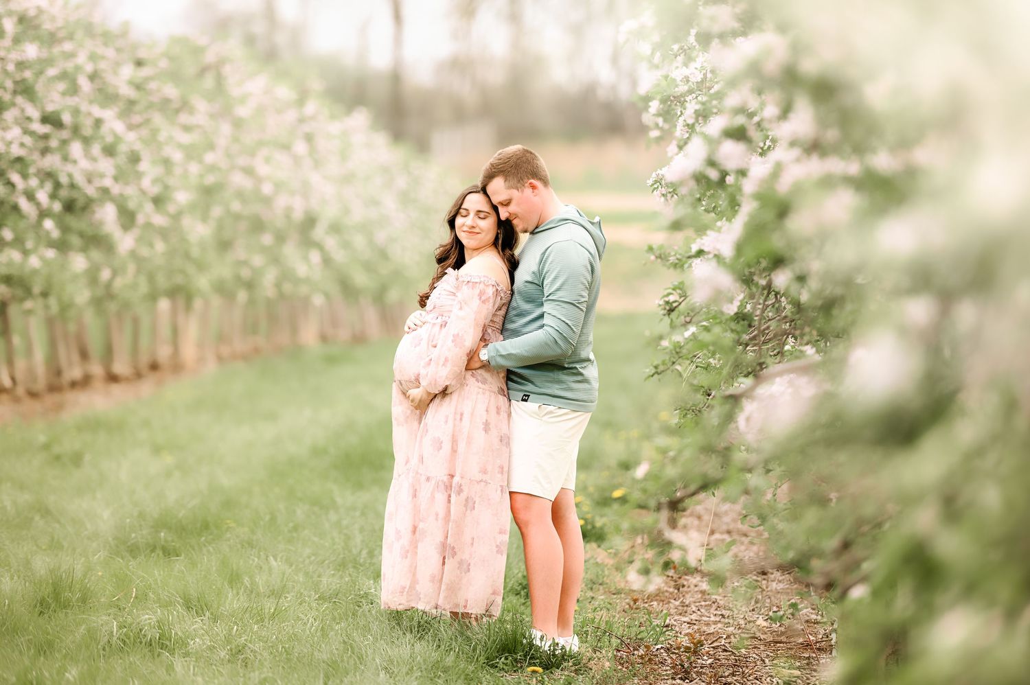 Romantic couple embraces in blooming orchard during maternity photo session.
