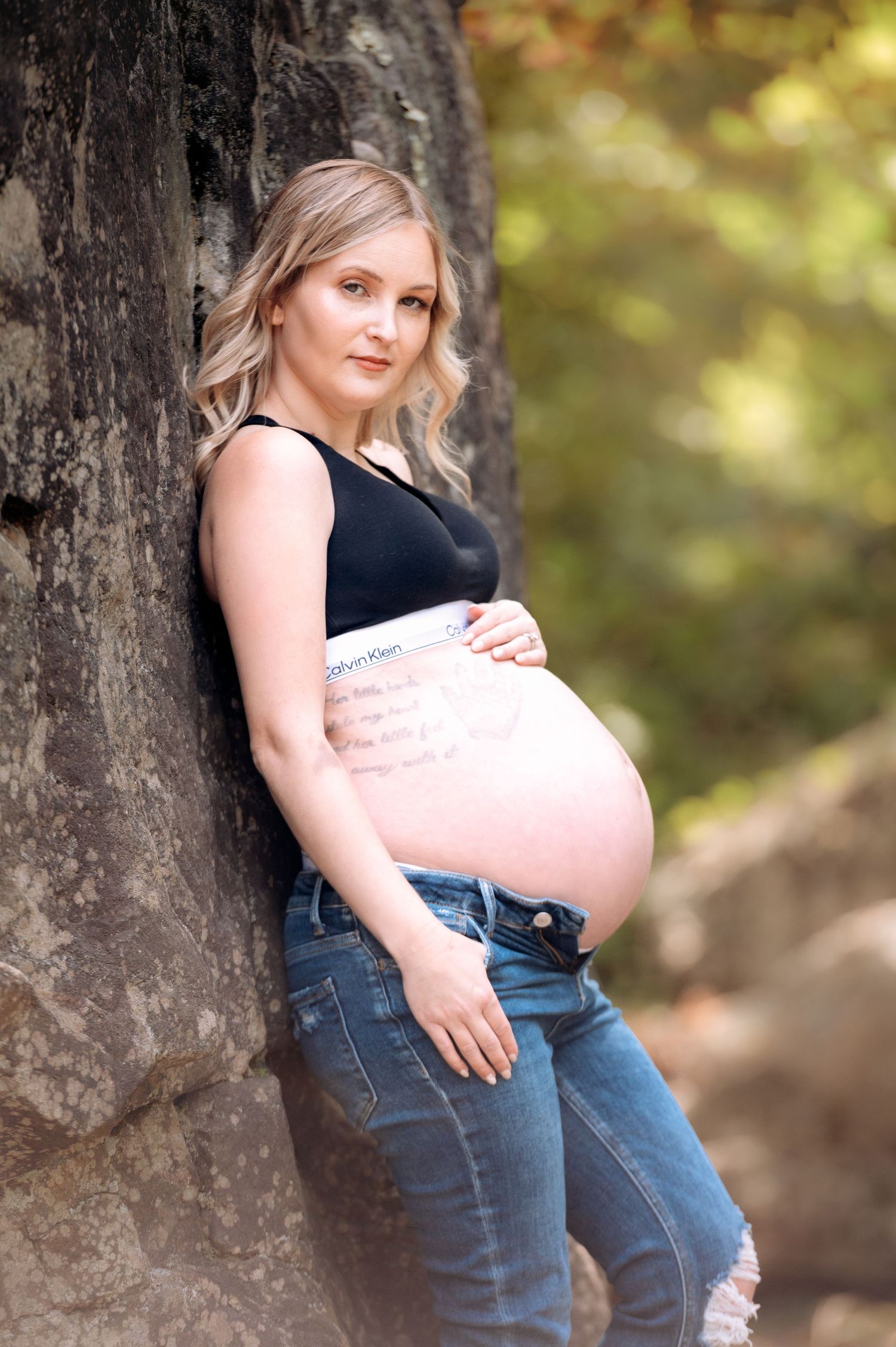 Casual maternity portrait against rock wall wearing jeans and black top.