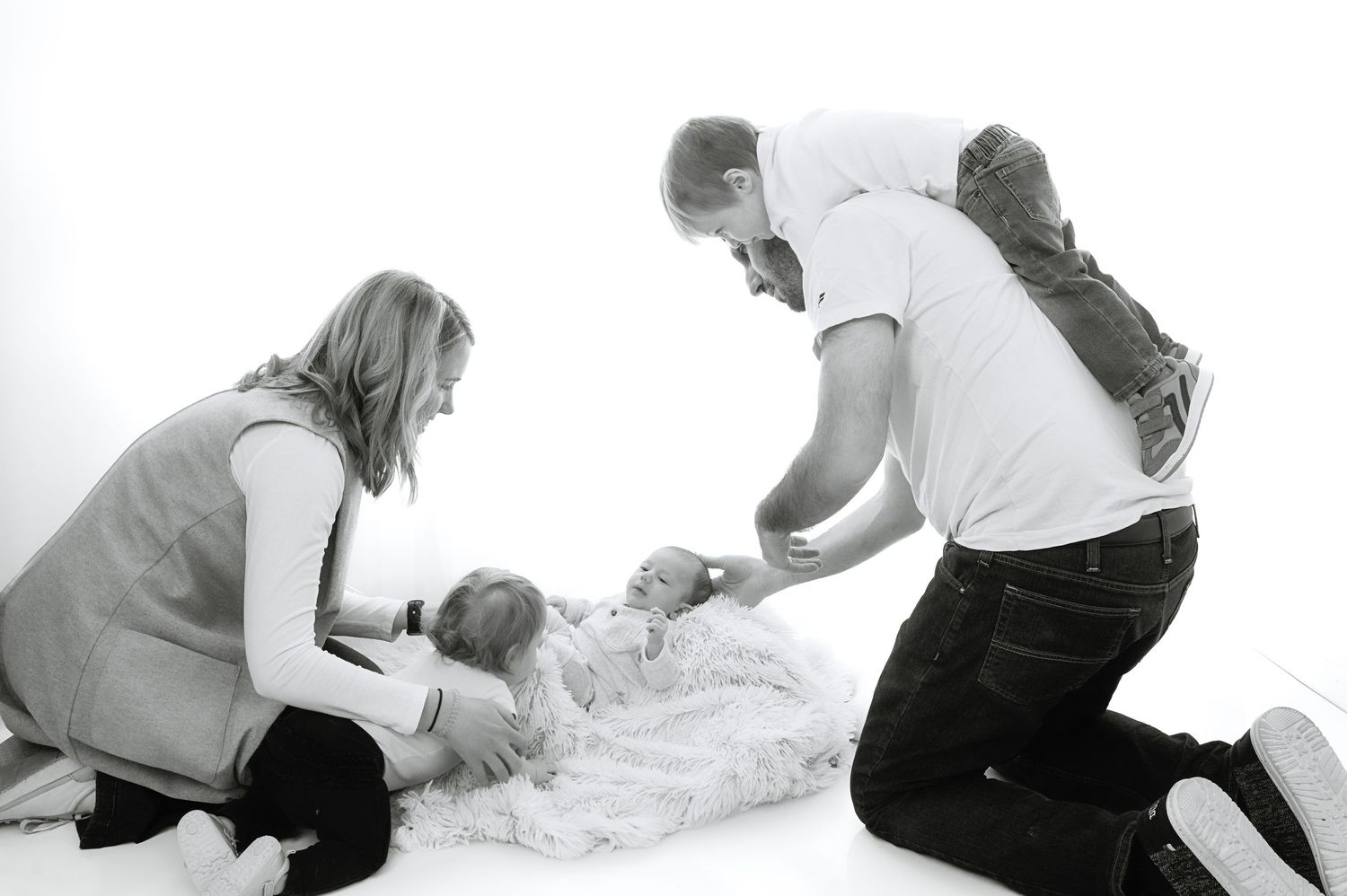 Black and white image of parents interacting with baby on soft blanket during photo session.