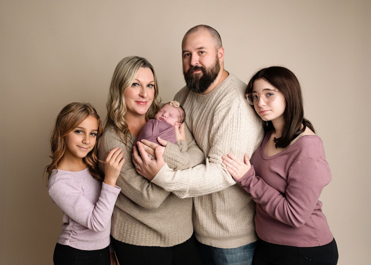 Family group portrait in neutral tones against beige backdrop showing playful interaction.
