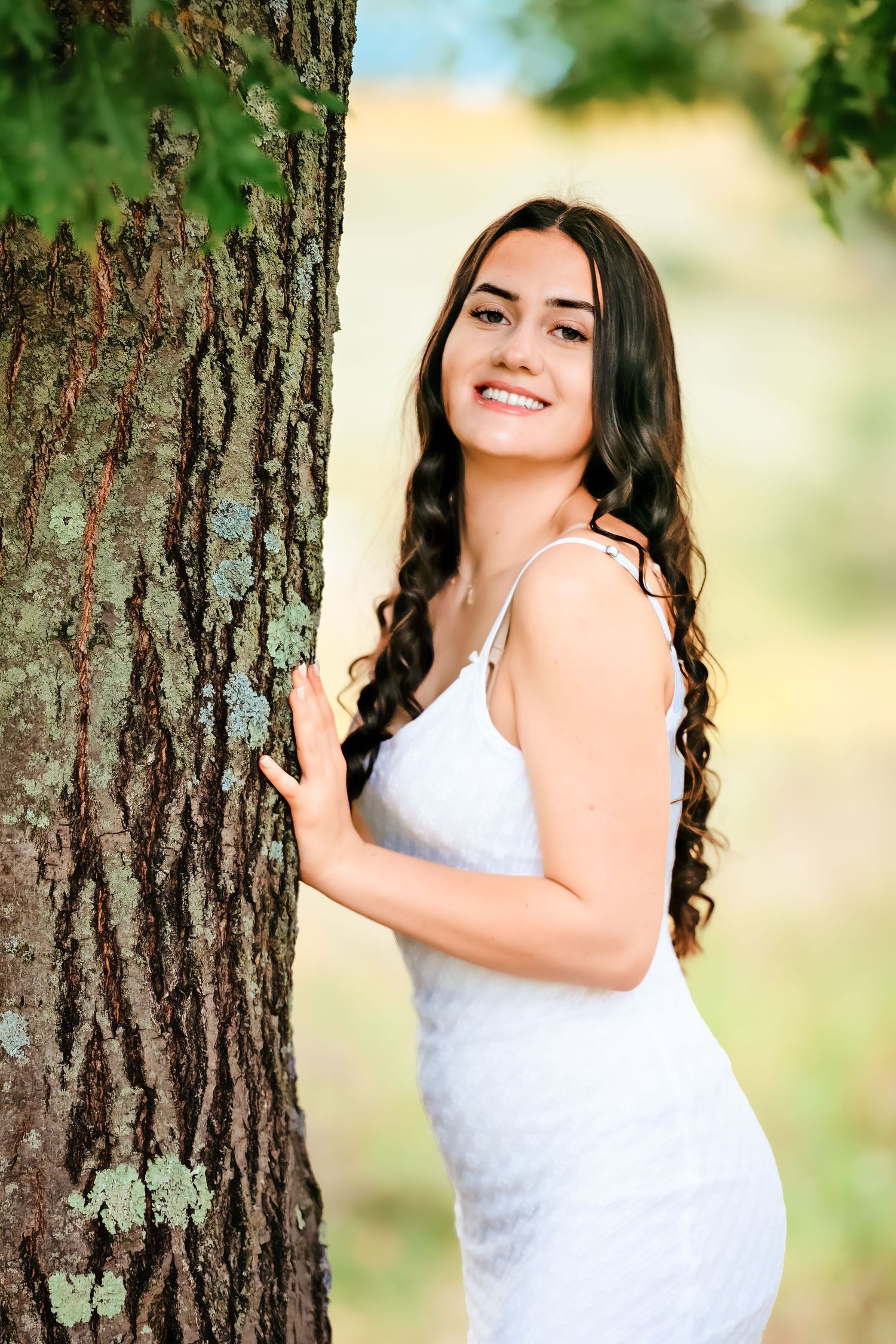 A white dress creates contrast against textured tree bark in a natural setting.