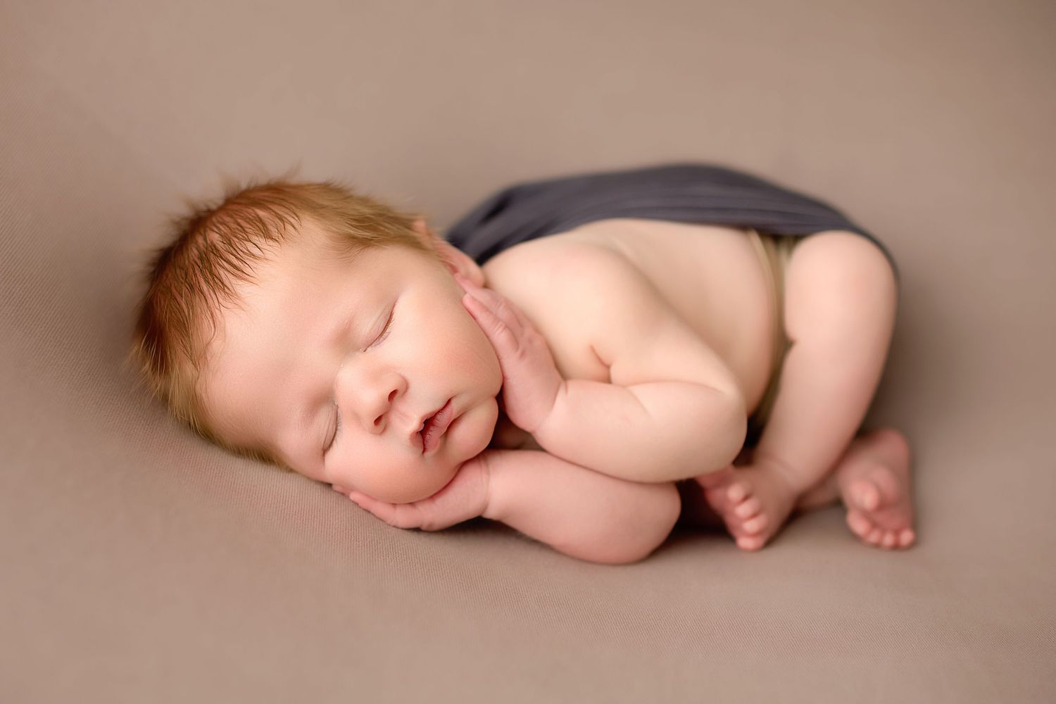 Sleeping newborn posed naturally on soft brown backdrop in minimalist style.