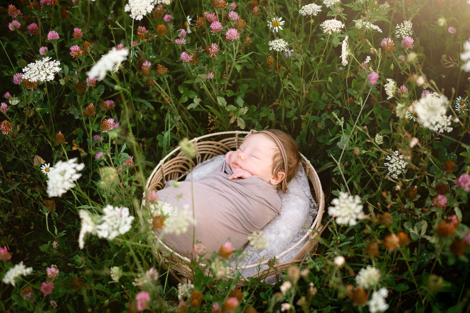 Artistic newborn photography setup with white flowers and pink swaddle in a garden setting.