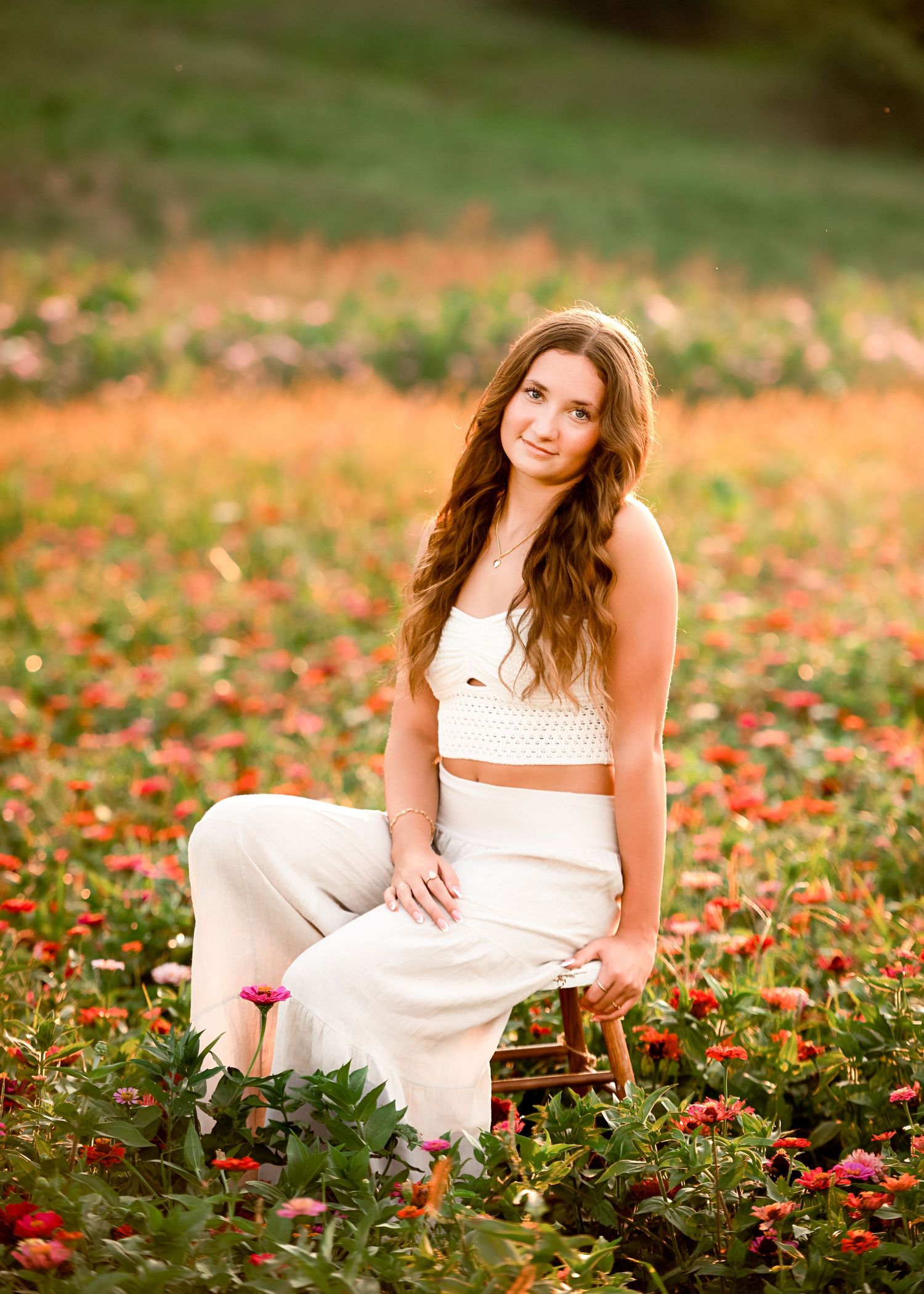 A person in a white dress sits gracefully among red flowers in a garden during golden hour lighting.