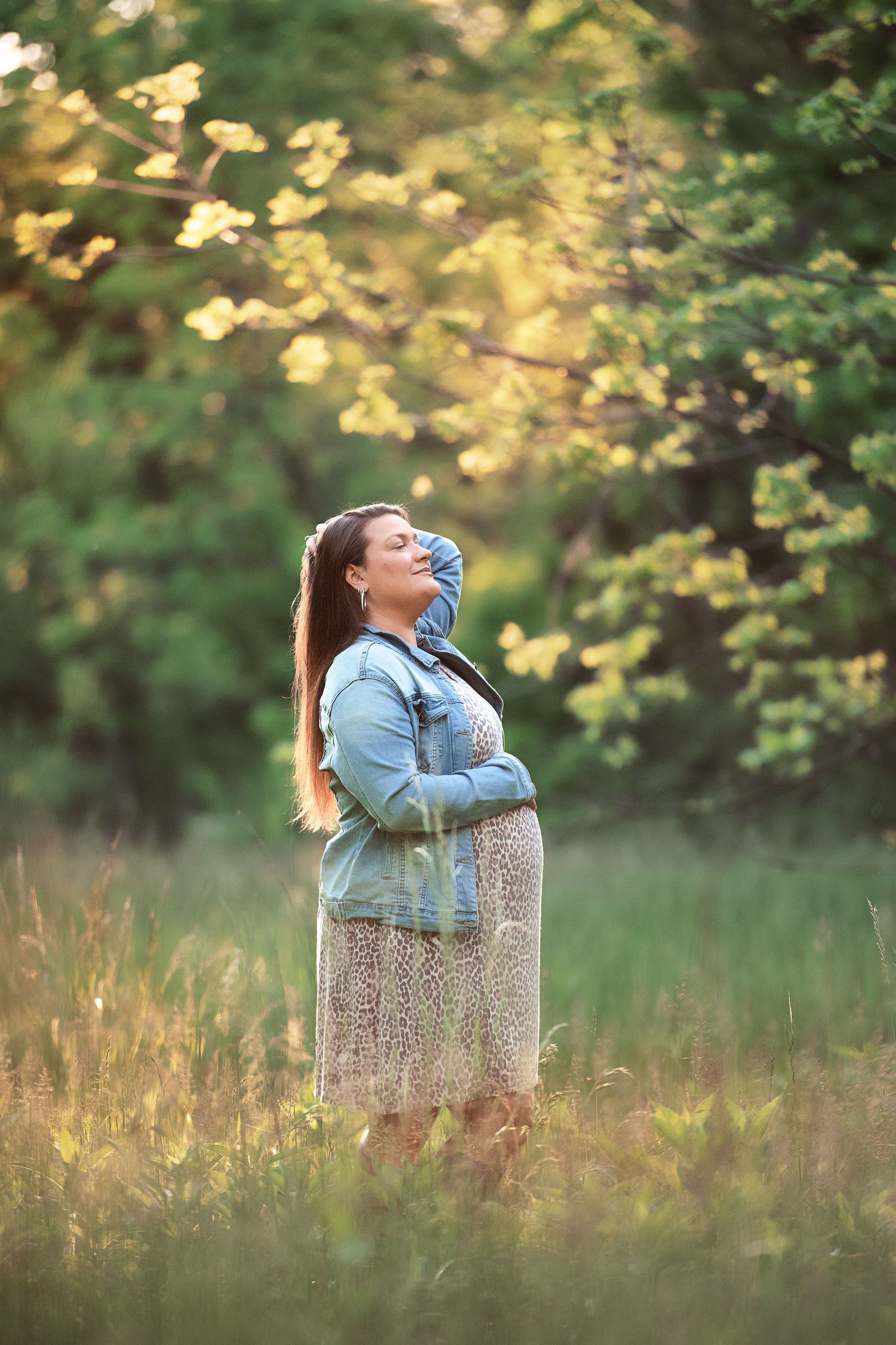 Person sitting on a decorative concrete pillar in a meadow during golden hour with trees in background.