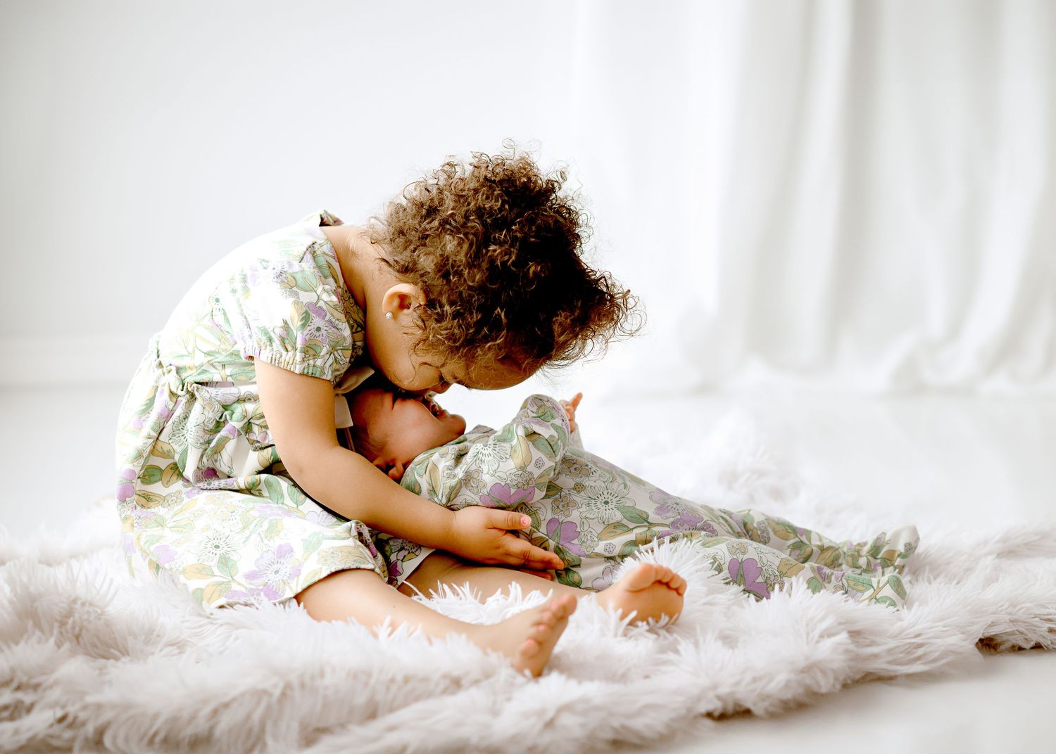 Young child playing with gray cat on white furry rug in bright setting.