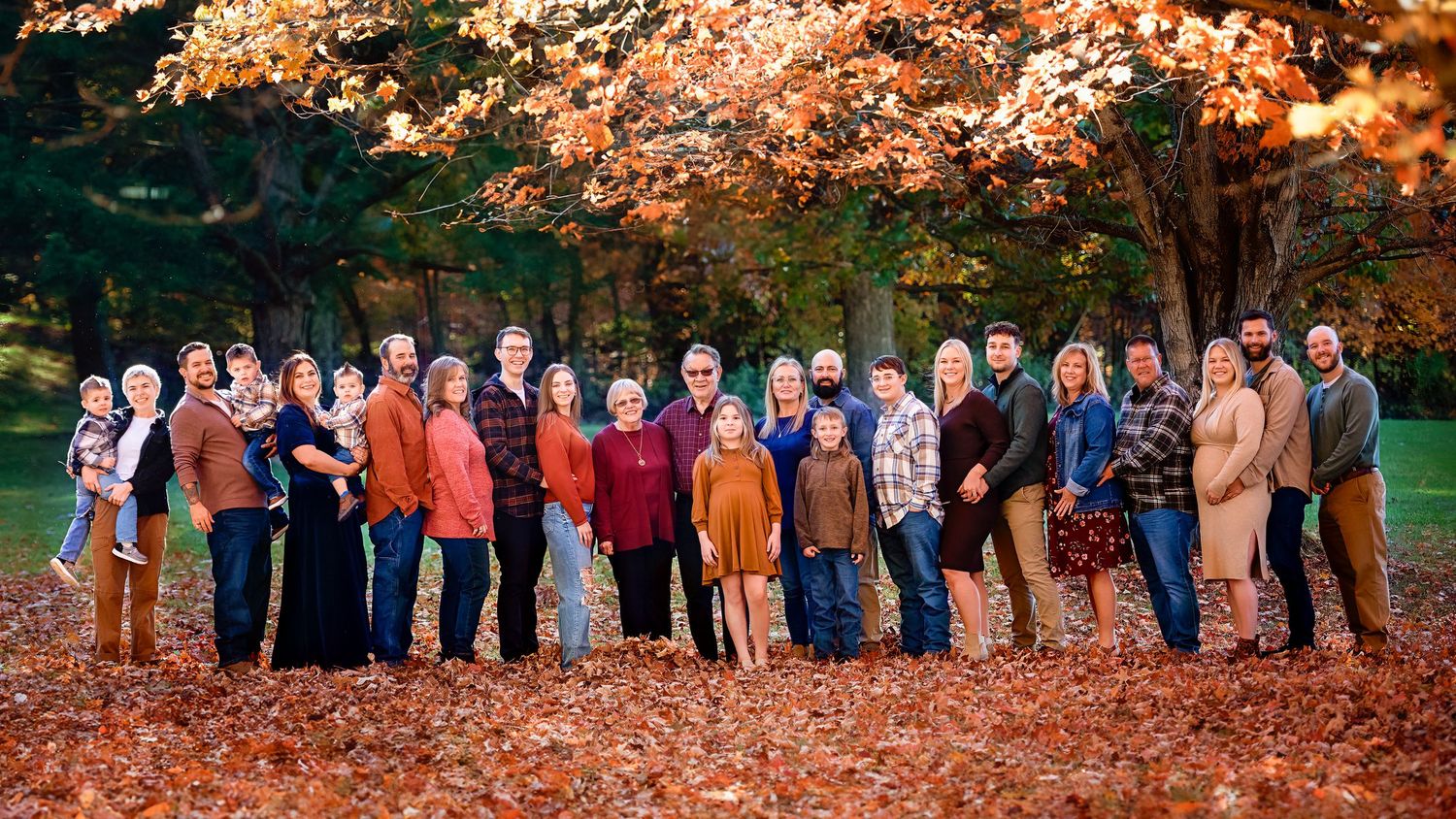Large extended family group photo outdoors with colorful fall foliage in the background.
