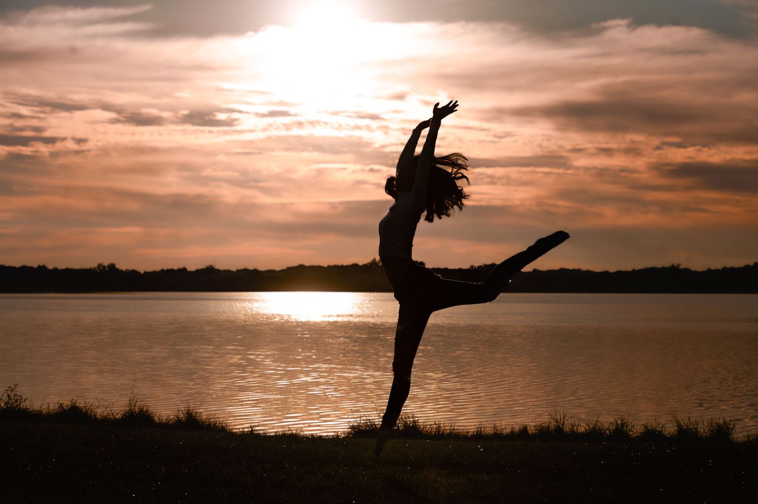 Silhouette of dancer performing against dramatic sunset over water.