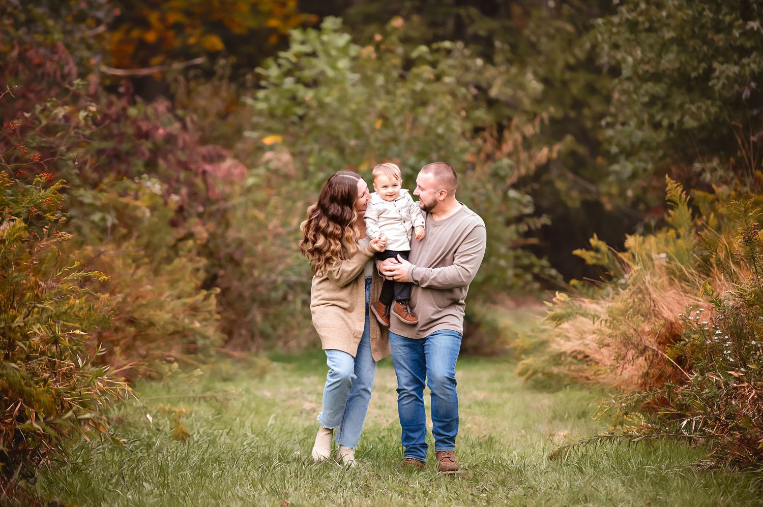 A family walks together through a scenic autumn forest path with colorful fall foliage surrounding them.