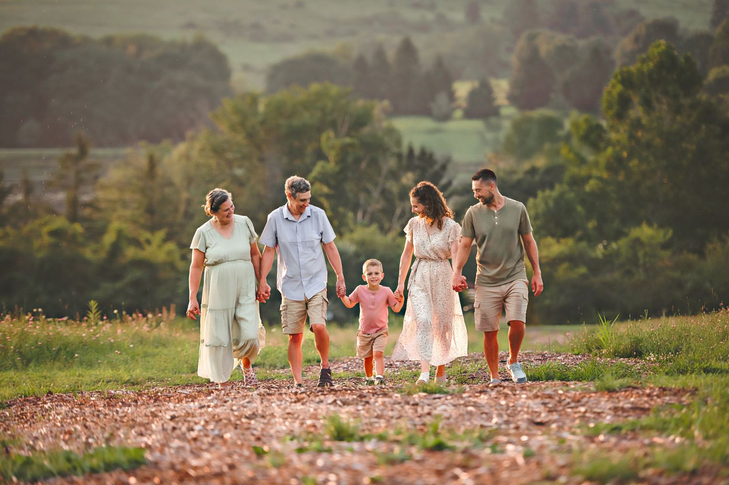Family walking together through a scenic hillside field during golden hour.