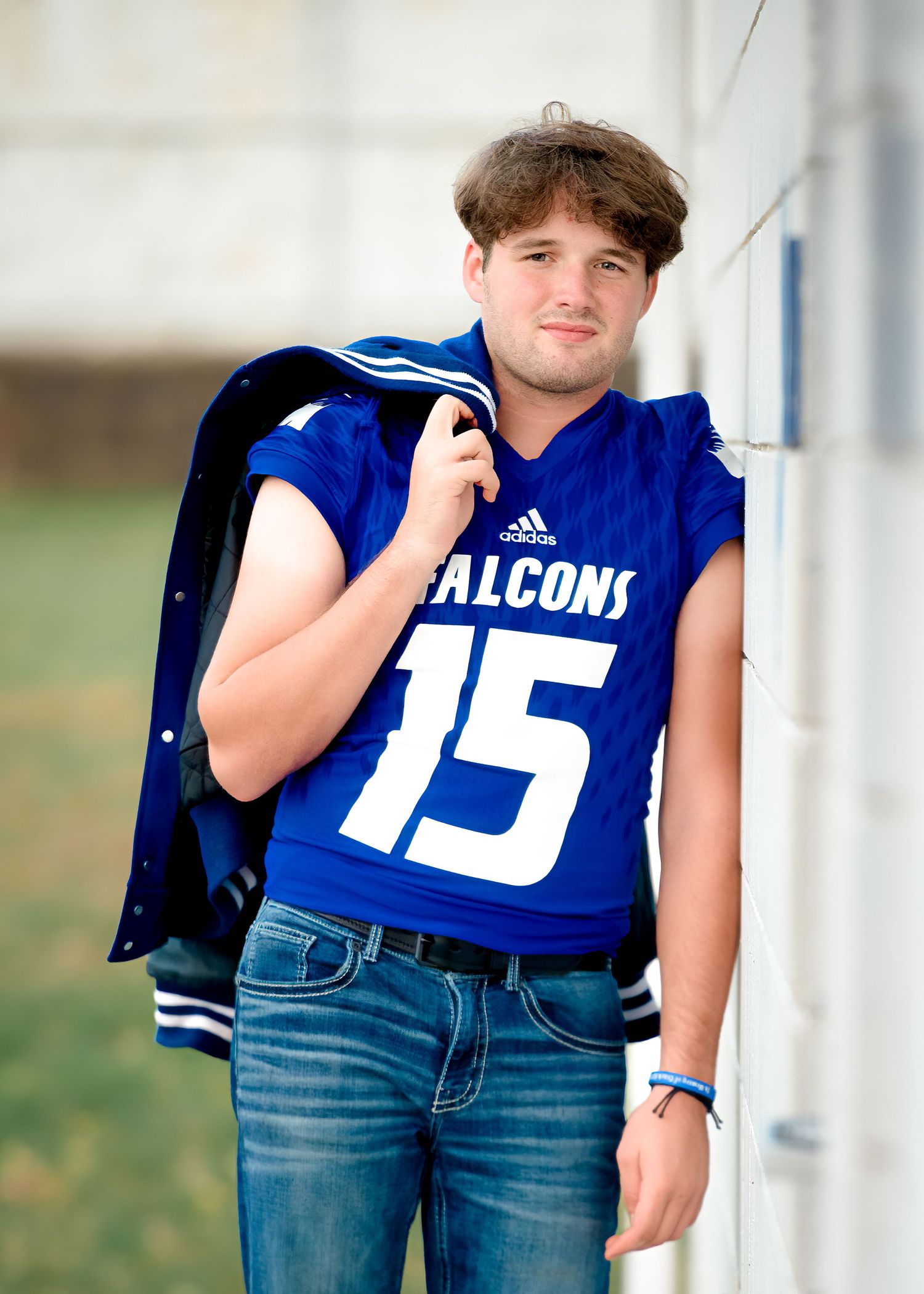 Football player wearing blue jersey number 15 leaning against white post.