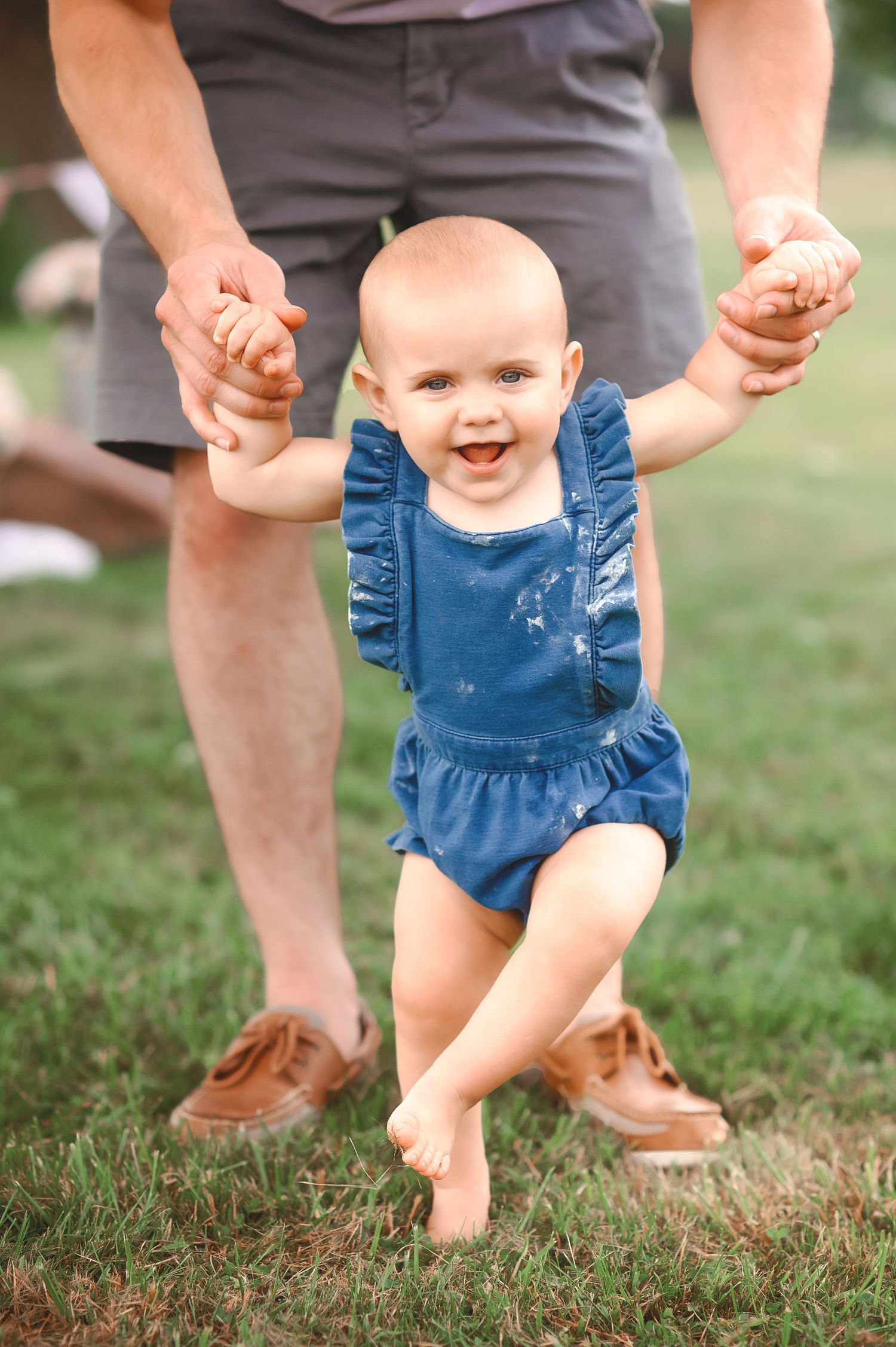 First steps on grass with supporting hands in blue denim outfit.