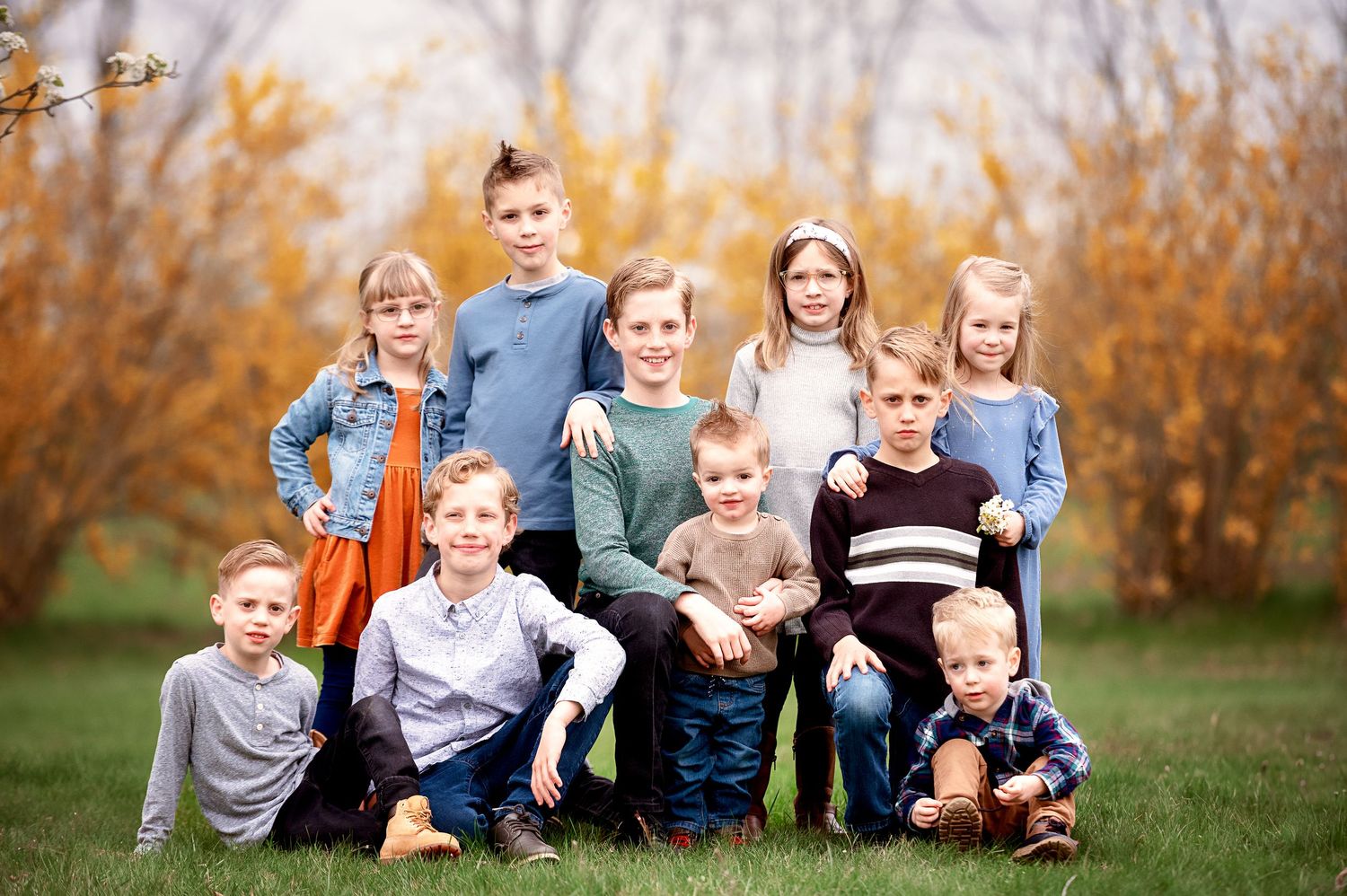Large family group poses together on grass during fall season photo shoot.