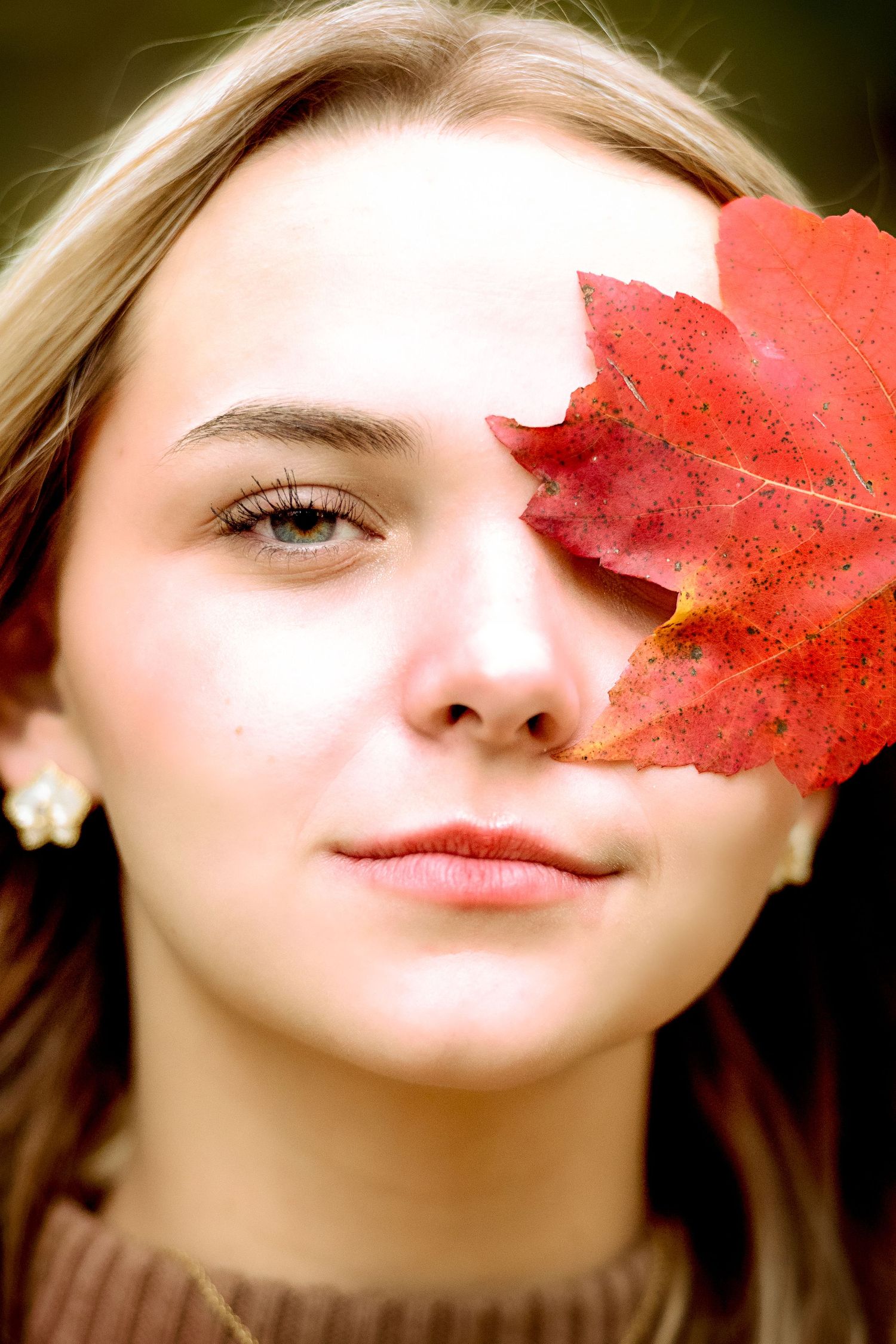 A creative portrait with a red autumn leaf partially covering the face.