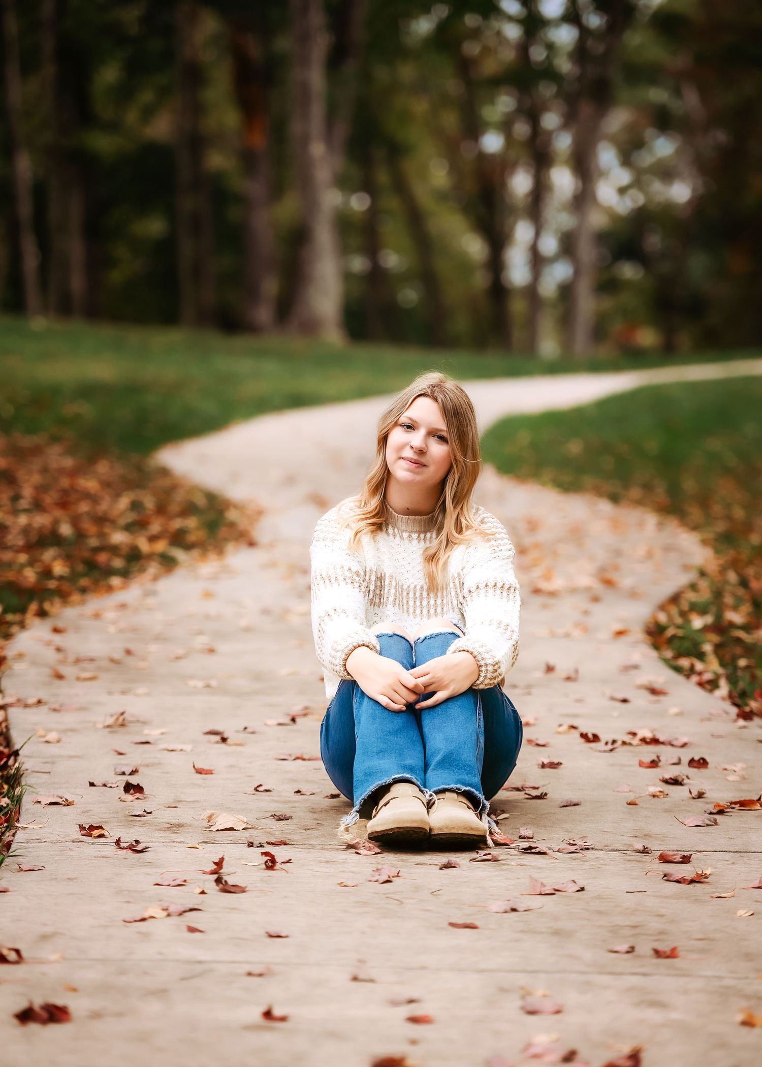 Autumn portrait on leaf-covered path wearing cream sweater and blue jeans.