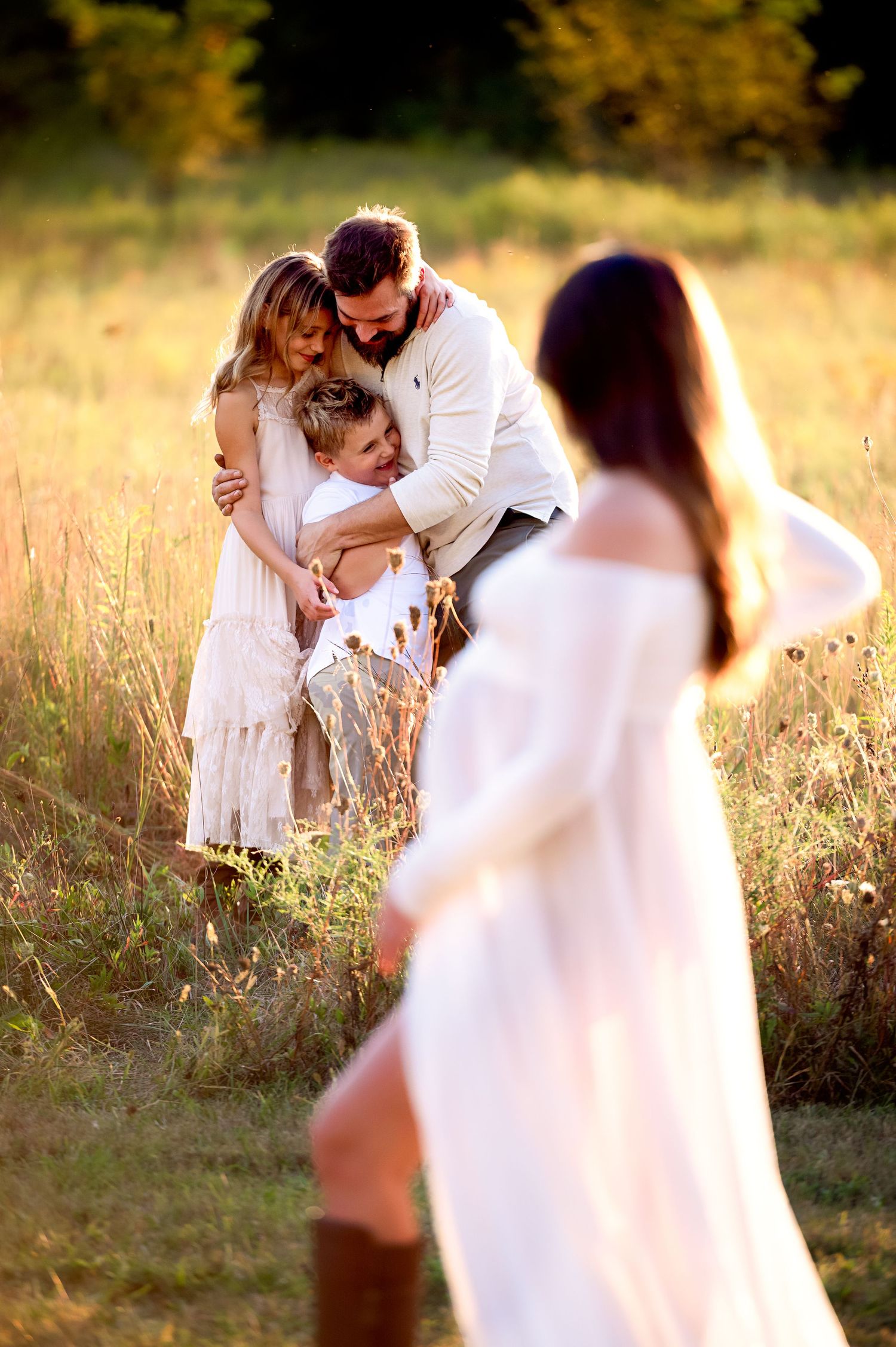 A family shares an intimate moment together in a sunlit field of tall golden grass at sunset.