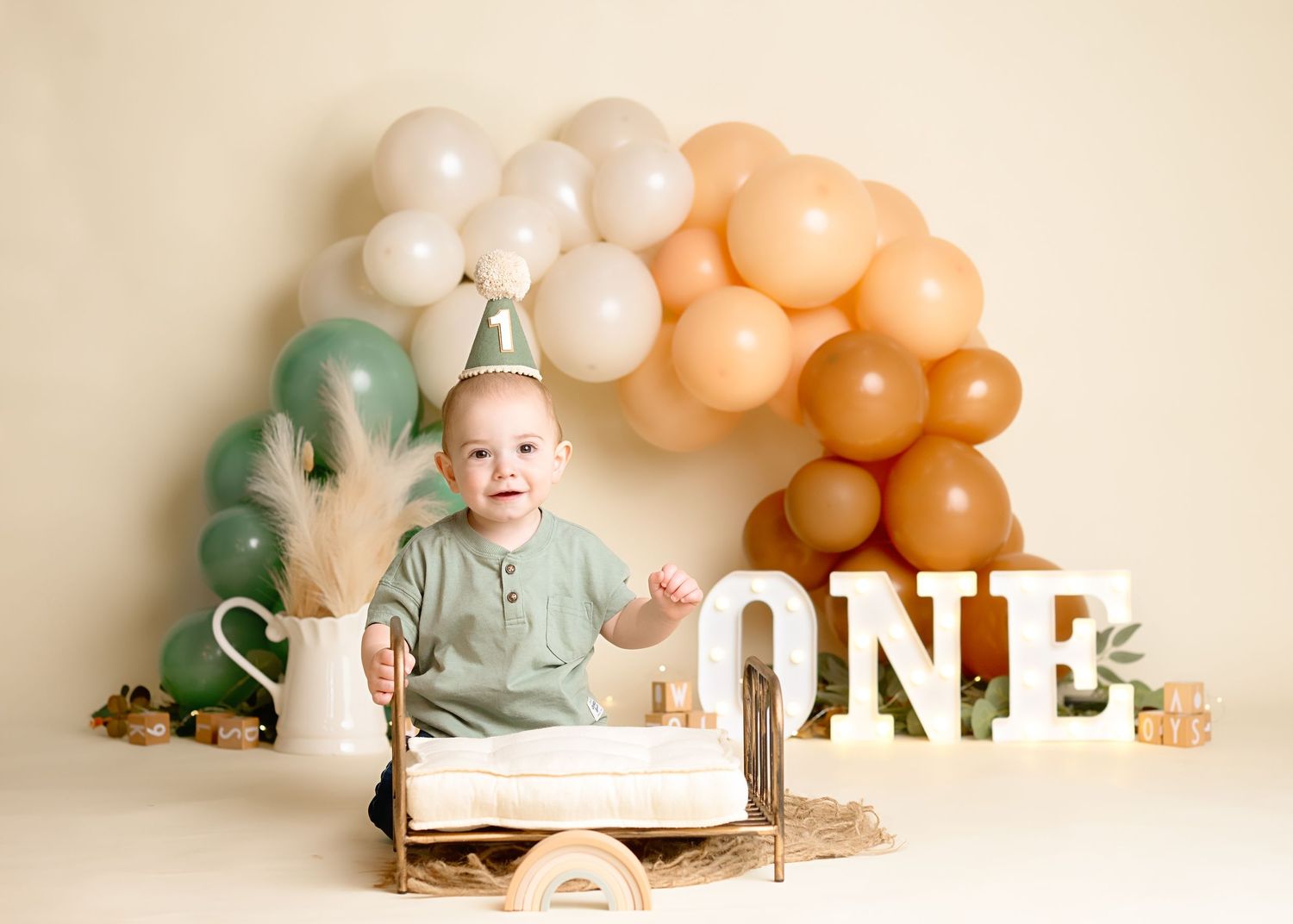 Neutral colored balloon arch with dinosaur decorations and cake setup for first birthday celebration.