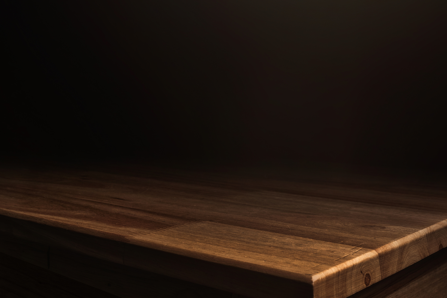Dark wooden table surface with rich grain texture, illuminated by soft spotlight against a dark background.
