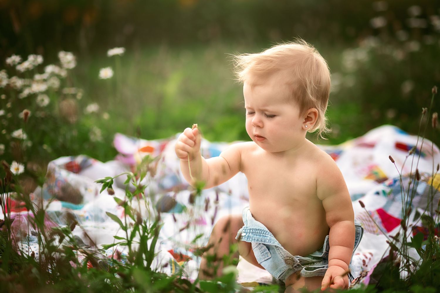 Baby plays among scattered flower petals during outdoor summer photo session.
