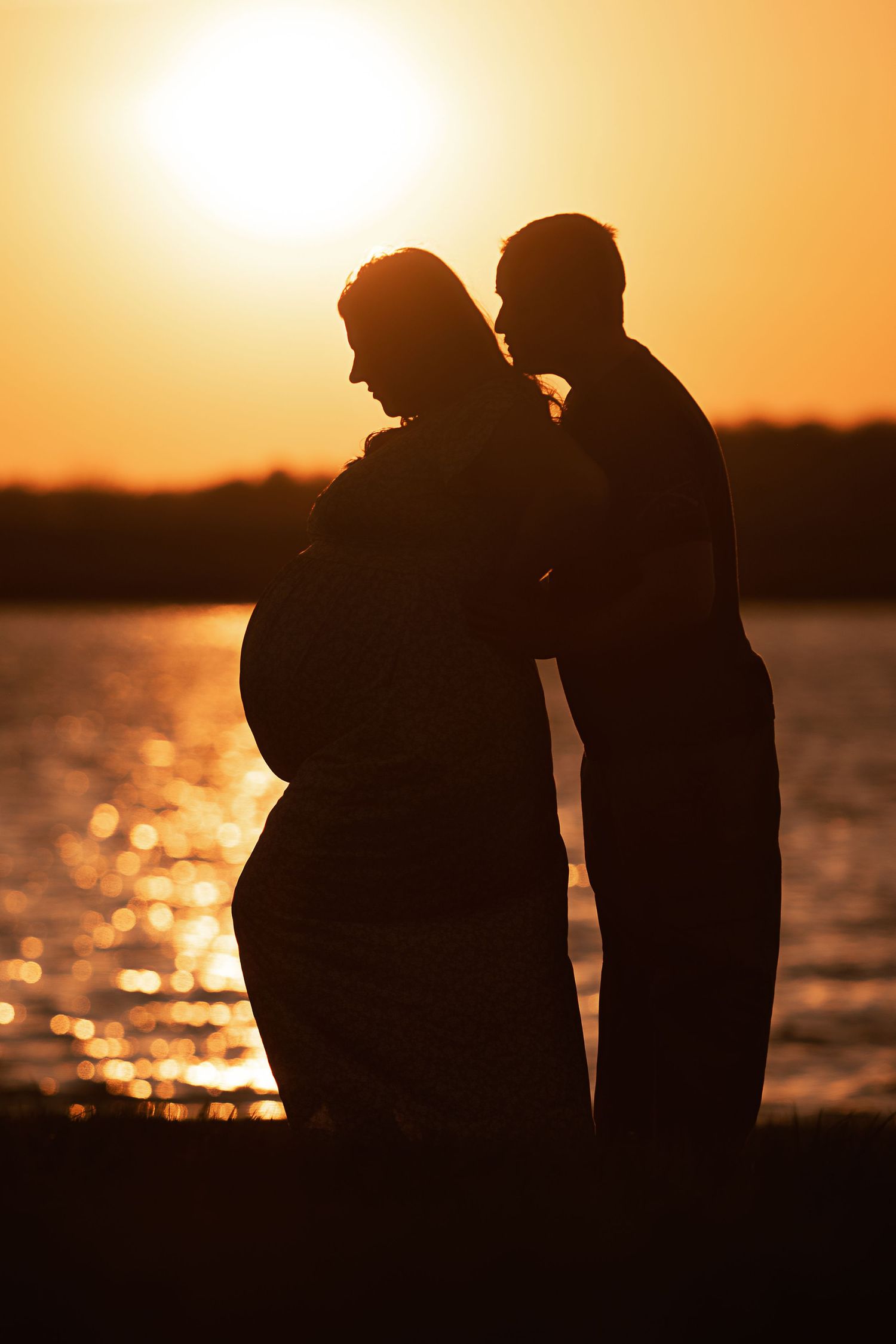 Silhouette of a couple by the water during sunset with dramatic orange sky.