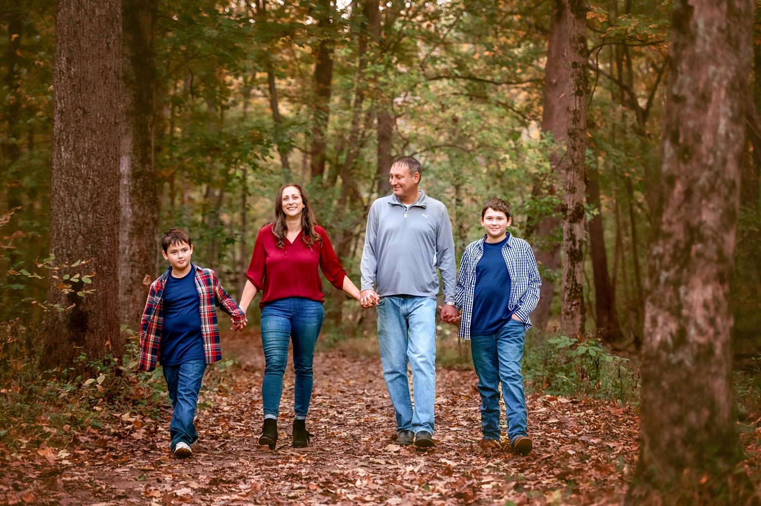 Group walking through wooded trail covered in fallen autumn leaves.
