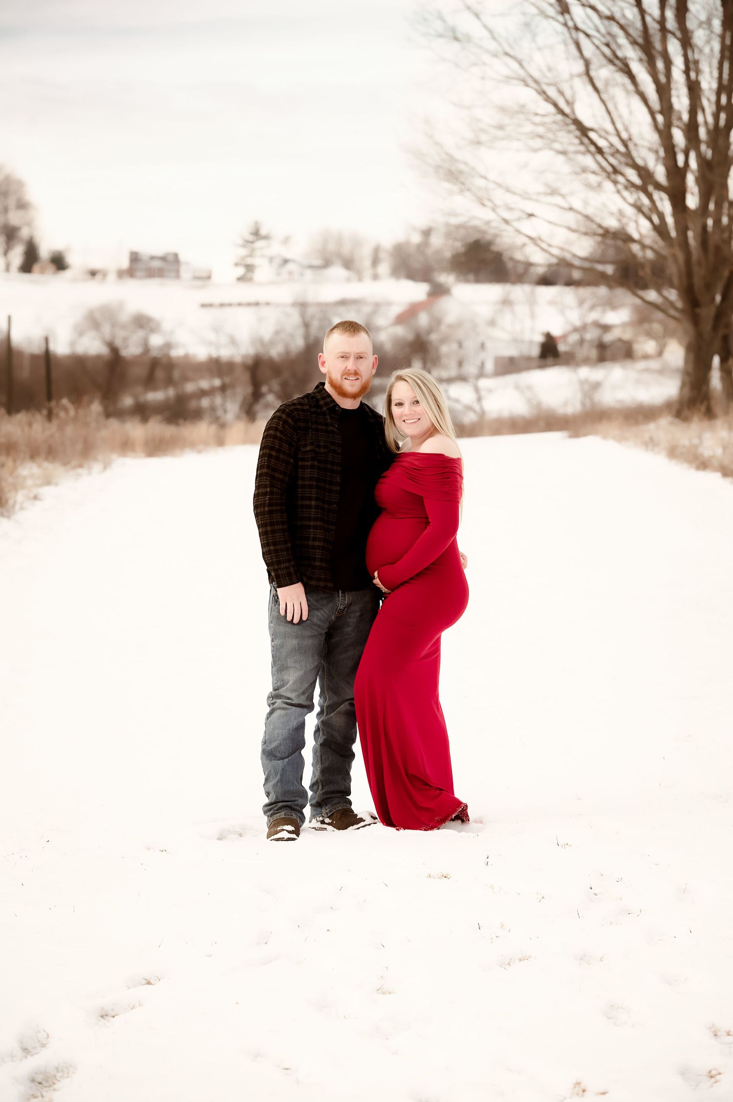 A romantic winter photoshoot in a snow-covered field with bare trees in the background.