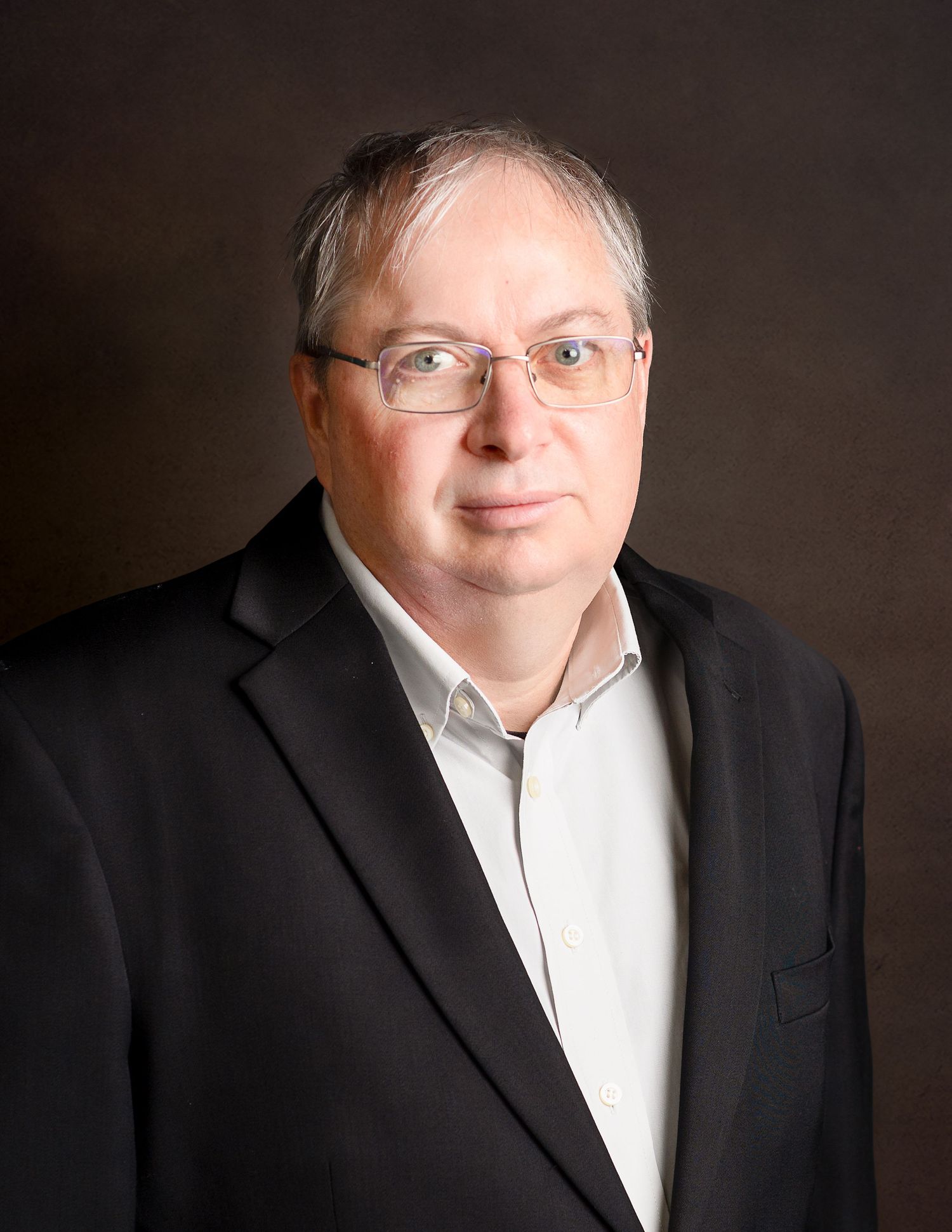 Executive portrait series of man in black blazer and white shirt against dark backdrop.