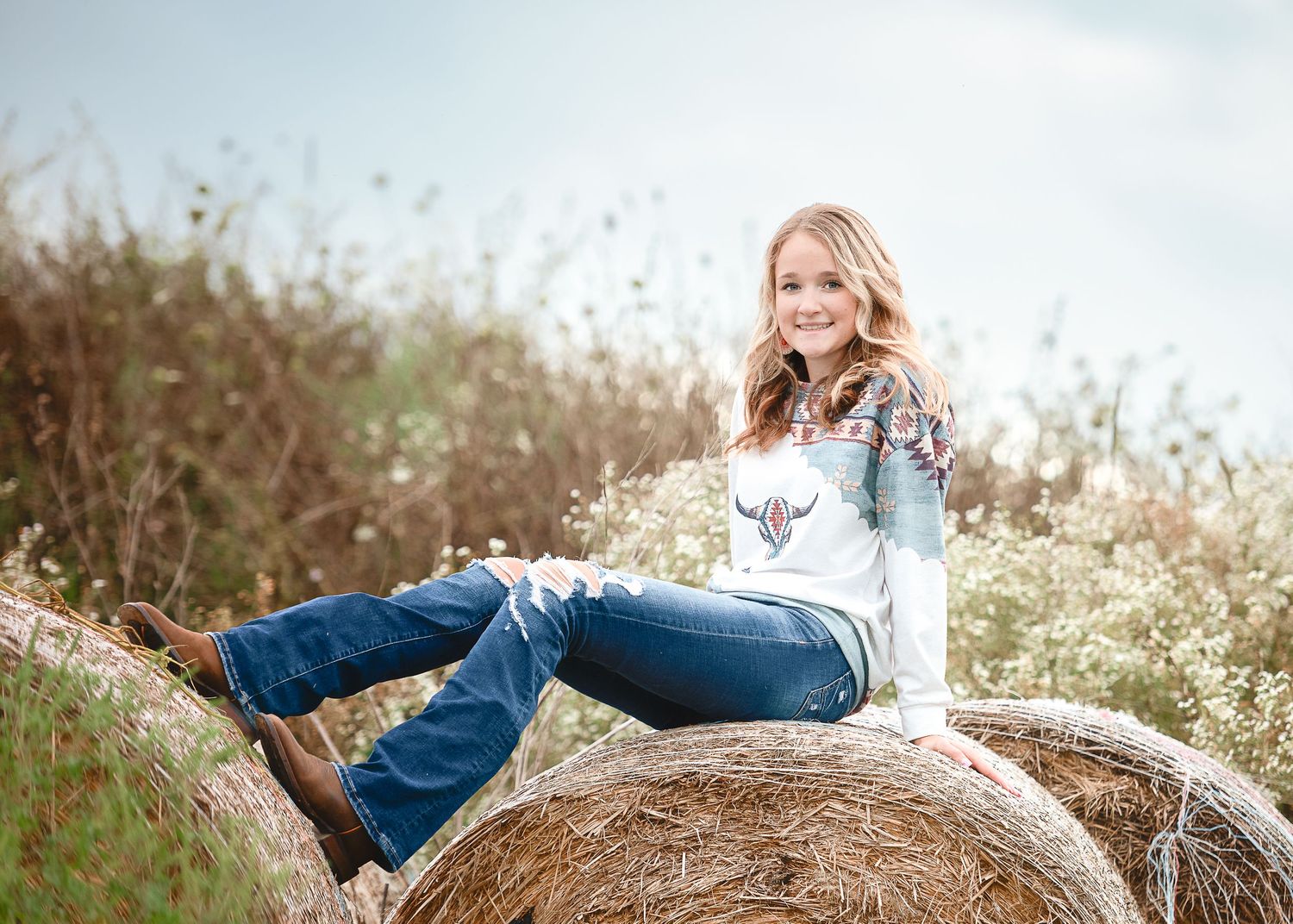 Person relaxing on a rustic hay bale in a sunny field.