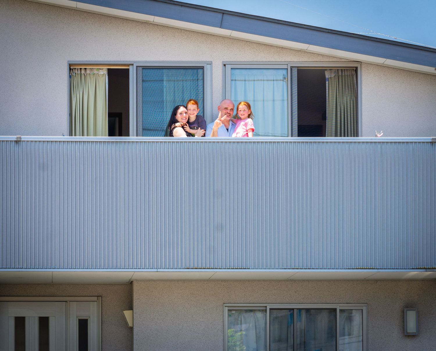 Family members peek out from hotel balcony on second floor of modern gray building.