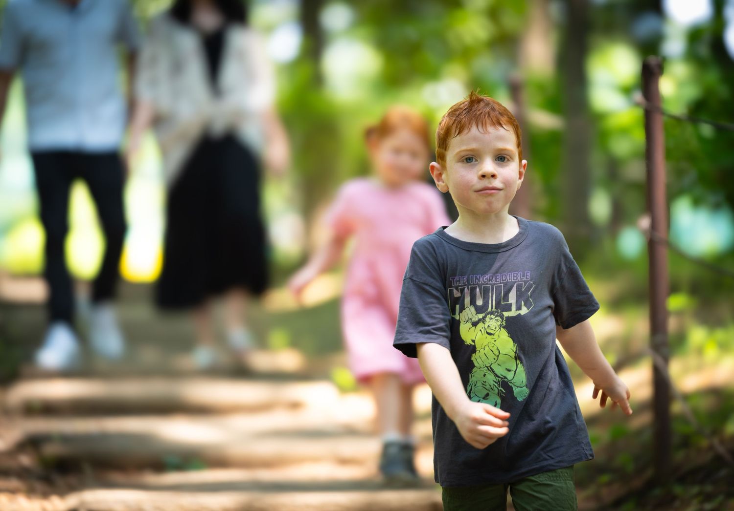 Child walks along a wooded nature path through a green forest in soft focus during a sunny summer day.