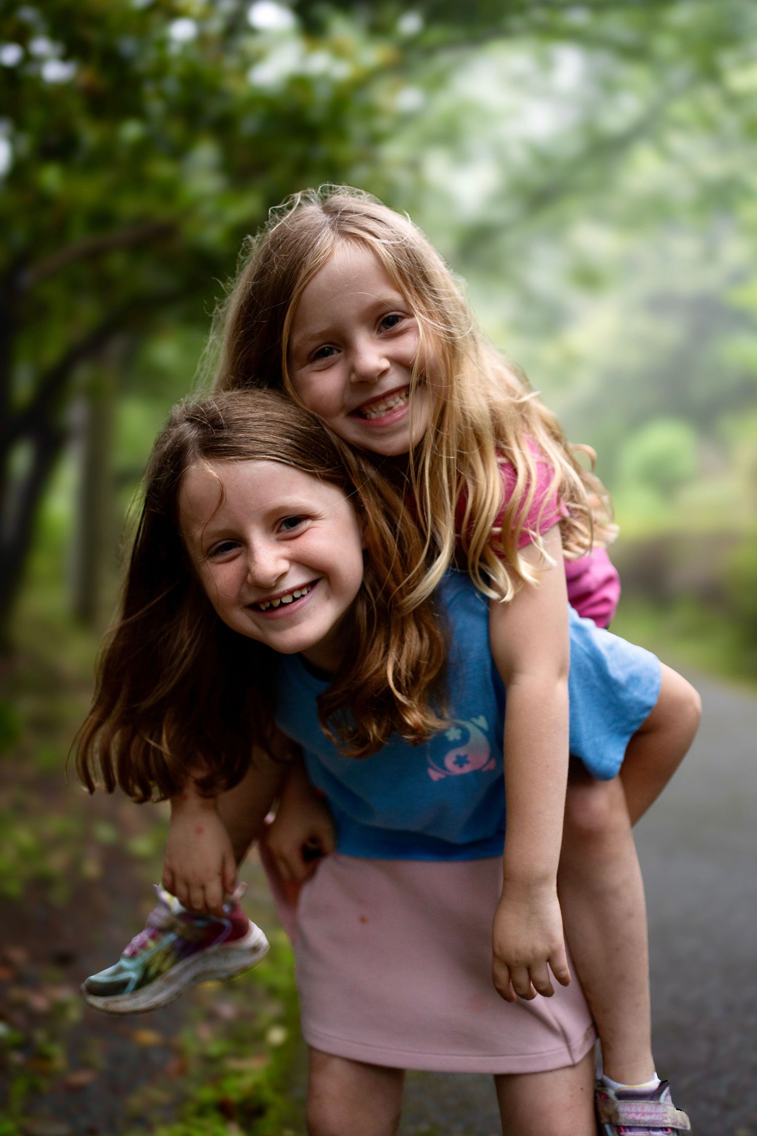 Two children having fun with piggyback ride on a wooded path.