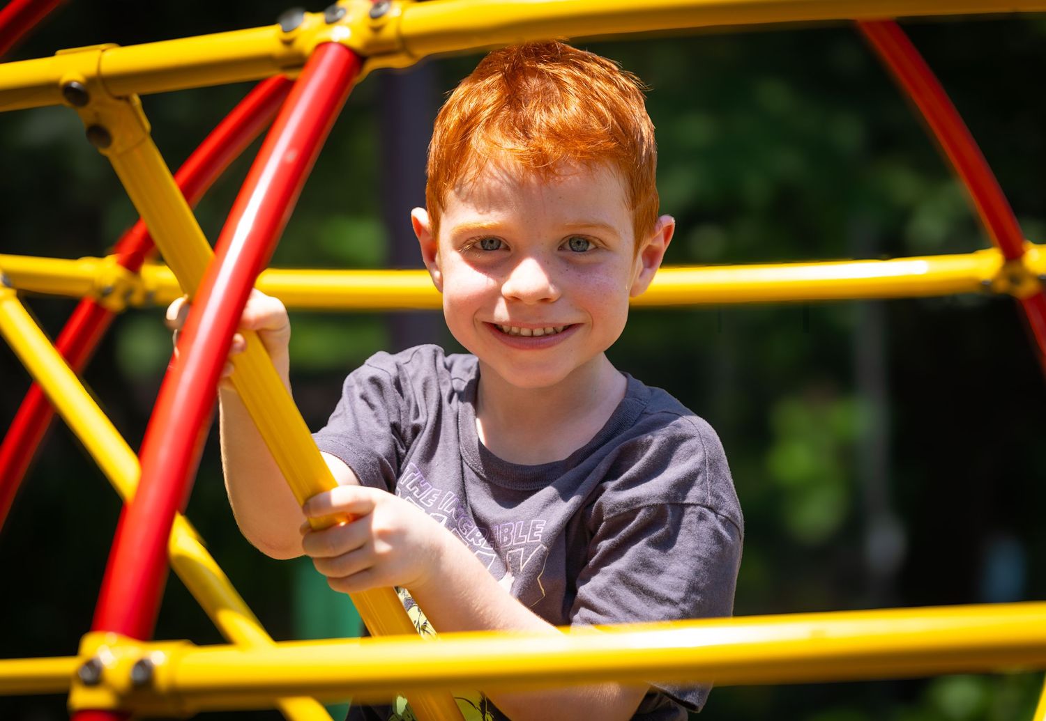 Small child plays on colorful playground monkey bars equipment on a bright sunny day.