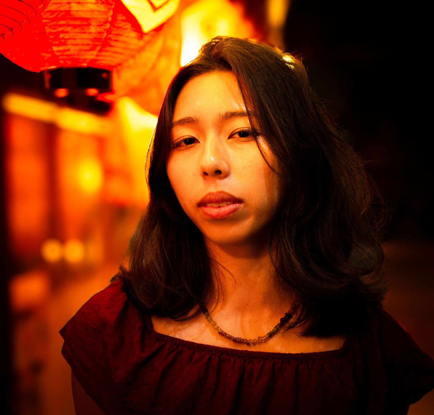 Portrait illuminated by warm orange lantern light in nighttime setting.