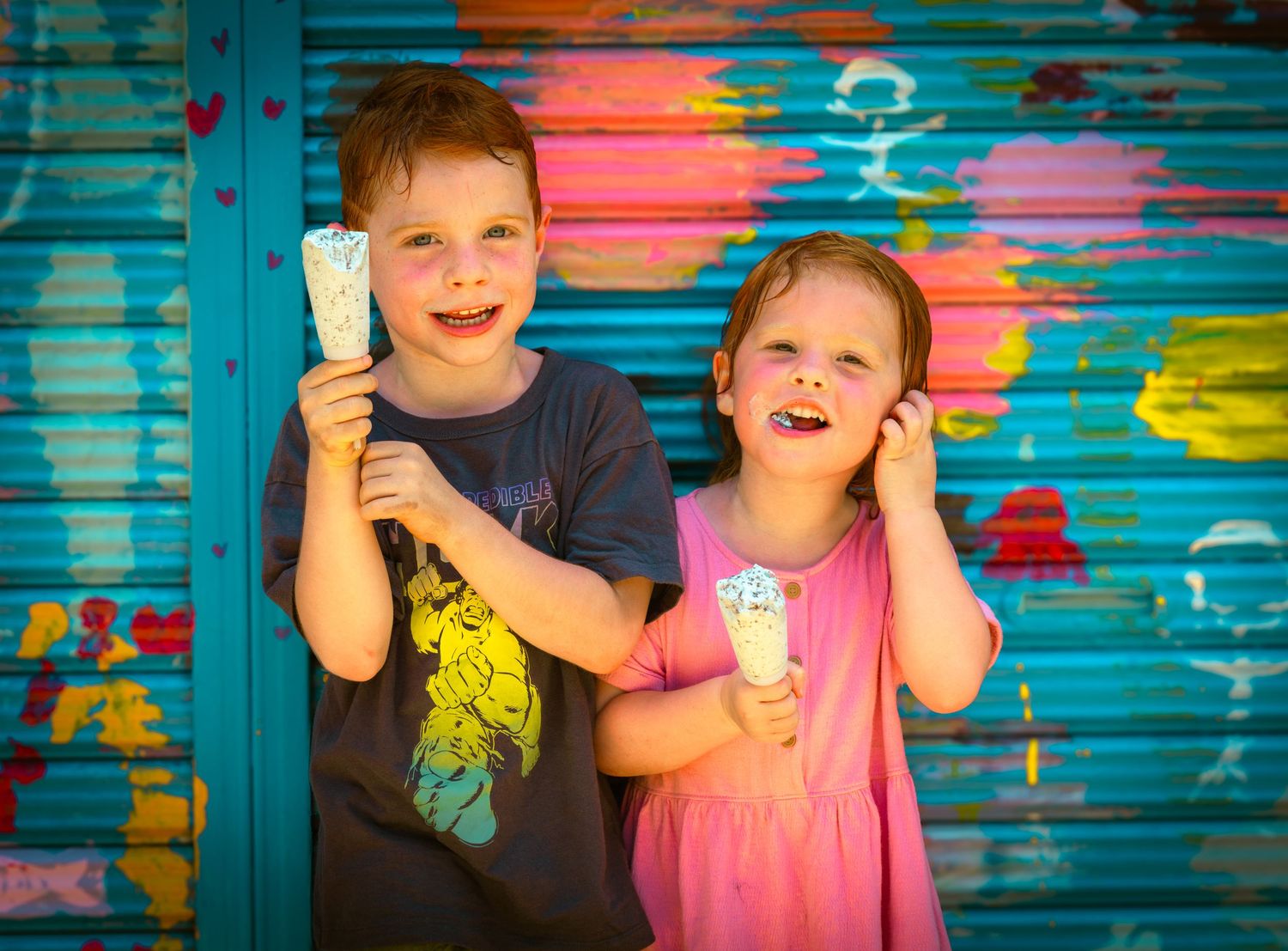 Children play together and laugh against colorful graffiti wall with bright blue and pink tones in background.